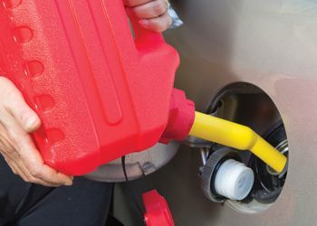 Person filling a car's gas tank with gasoline from a red fuel container, using a yellow nozzle.