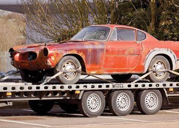 A rusty red vintage Volvo coupe being transported on a flatbed trailer.