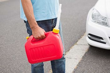 Man holding a red gas can beside a white car on a road.