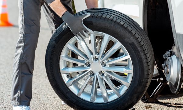Person in gray overalls changes a tire on a car on a road.