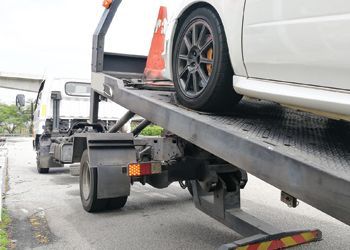A white car being loaded onto a tow truck, with an orange traffic cone.