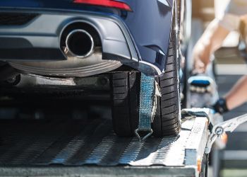 Blue car being secured onto a tow truck with straps.