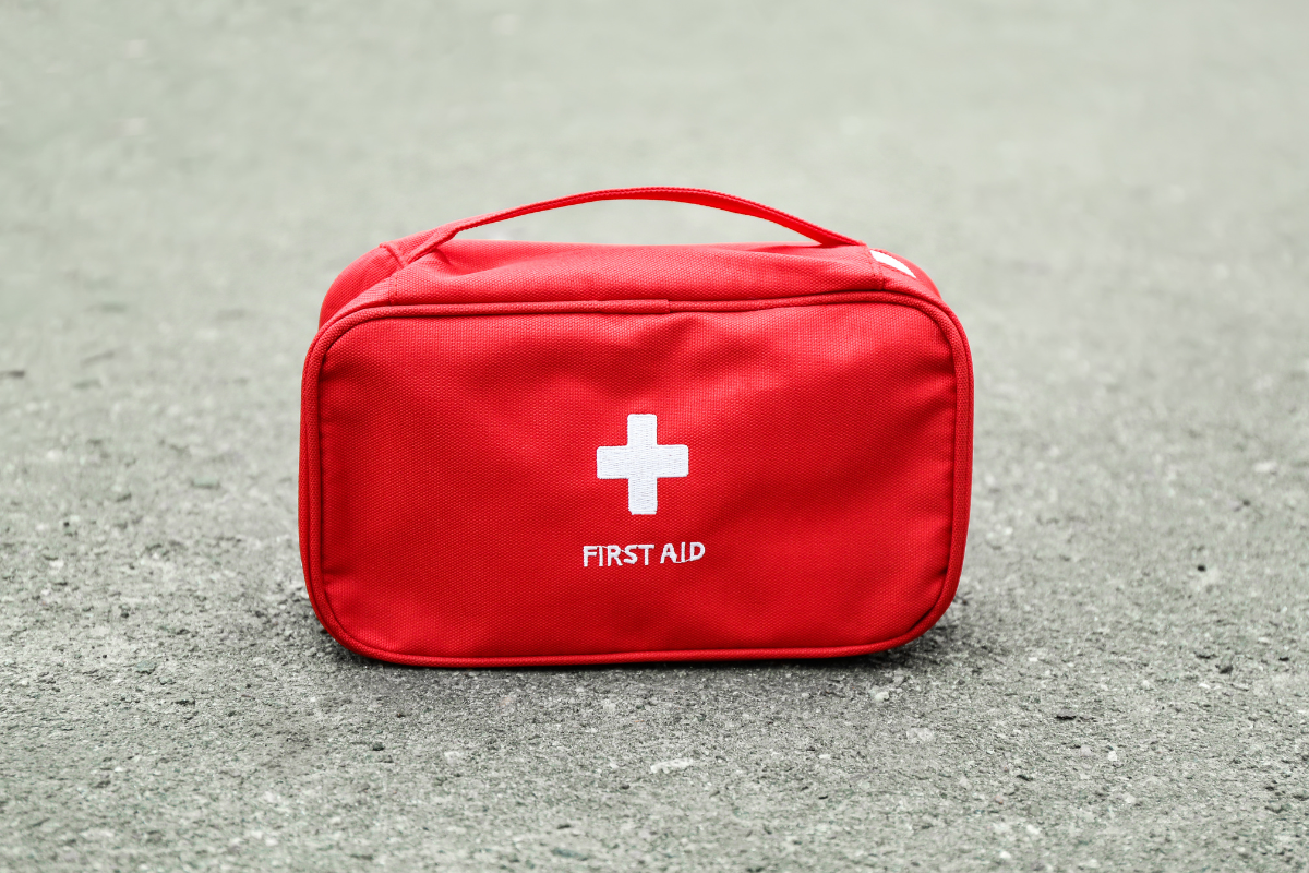 Red first aid kit with a white cross on a gray surface.