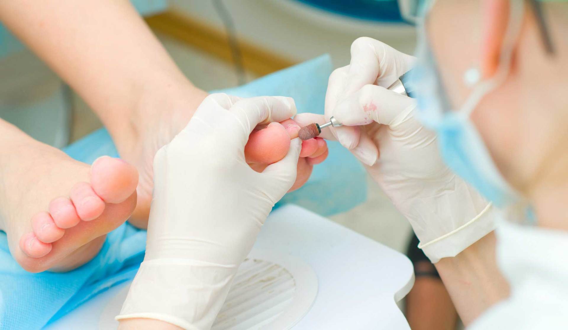 A healthcare professional in blue scrubs uses a handheld medical device to treat a patient’s foot in a clinic.