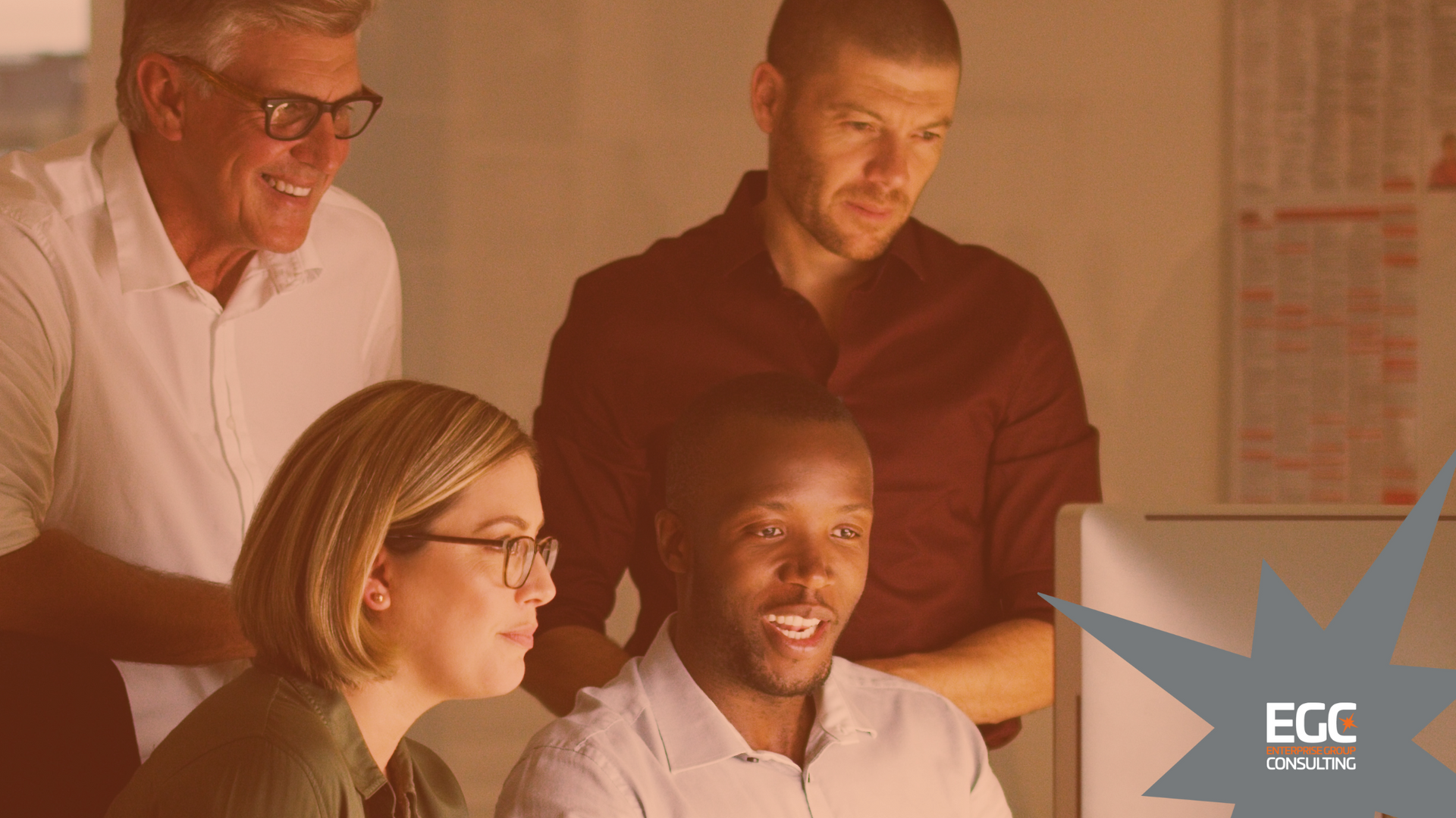 Group of colleagues looking at a computer screen, smiling and engaged in an office setting.