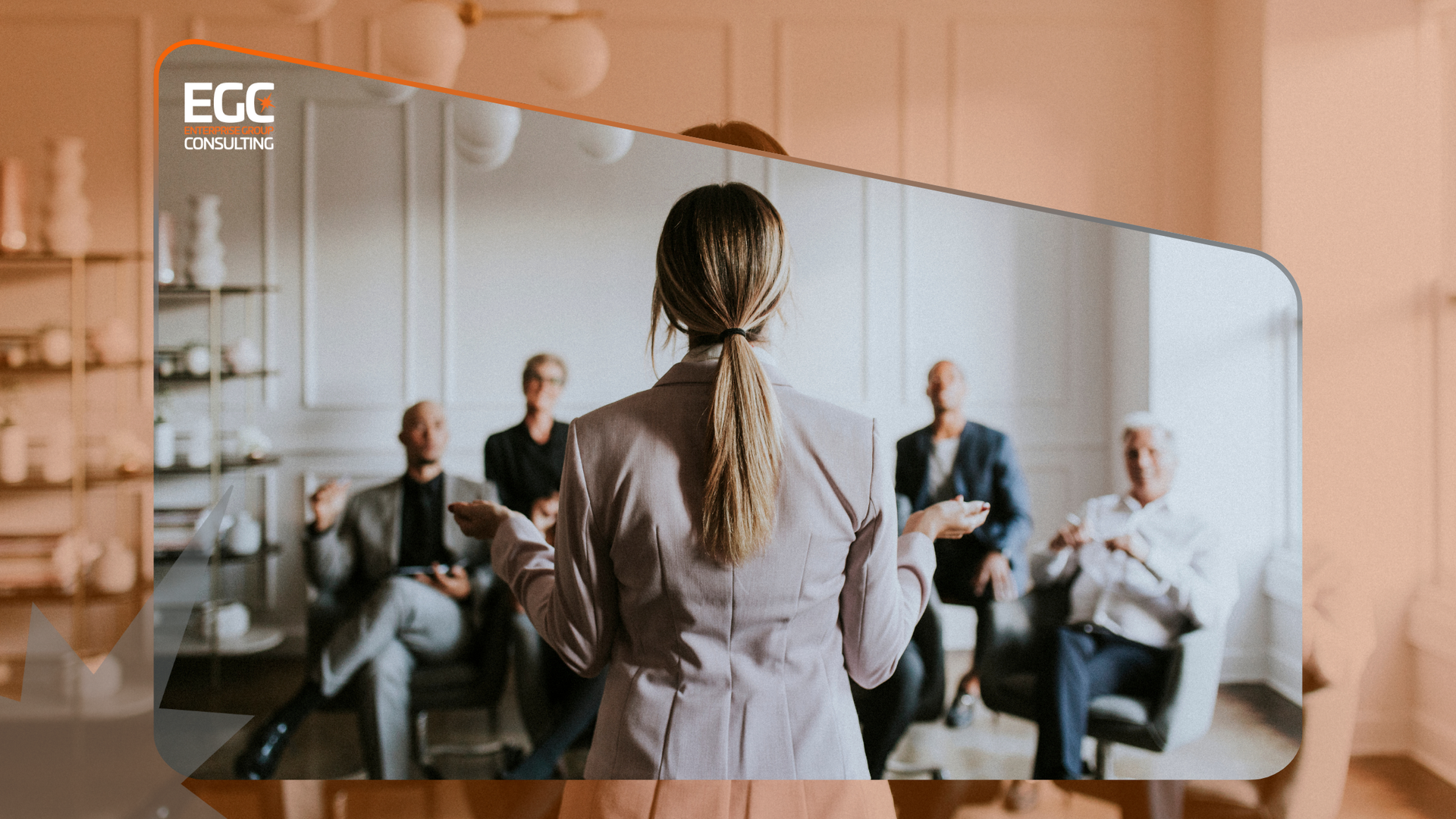 Woman giving a presentation to a seated group. Beige interior with neutral colors.