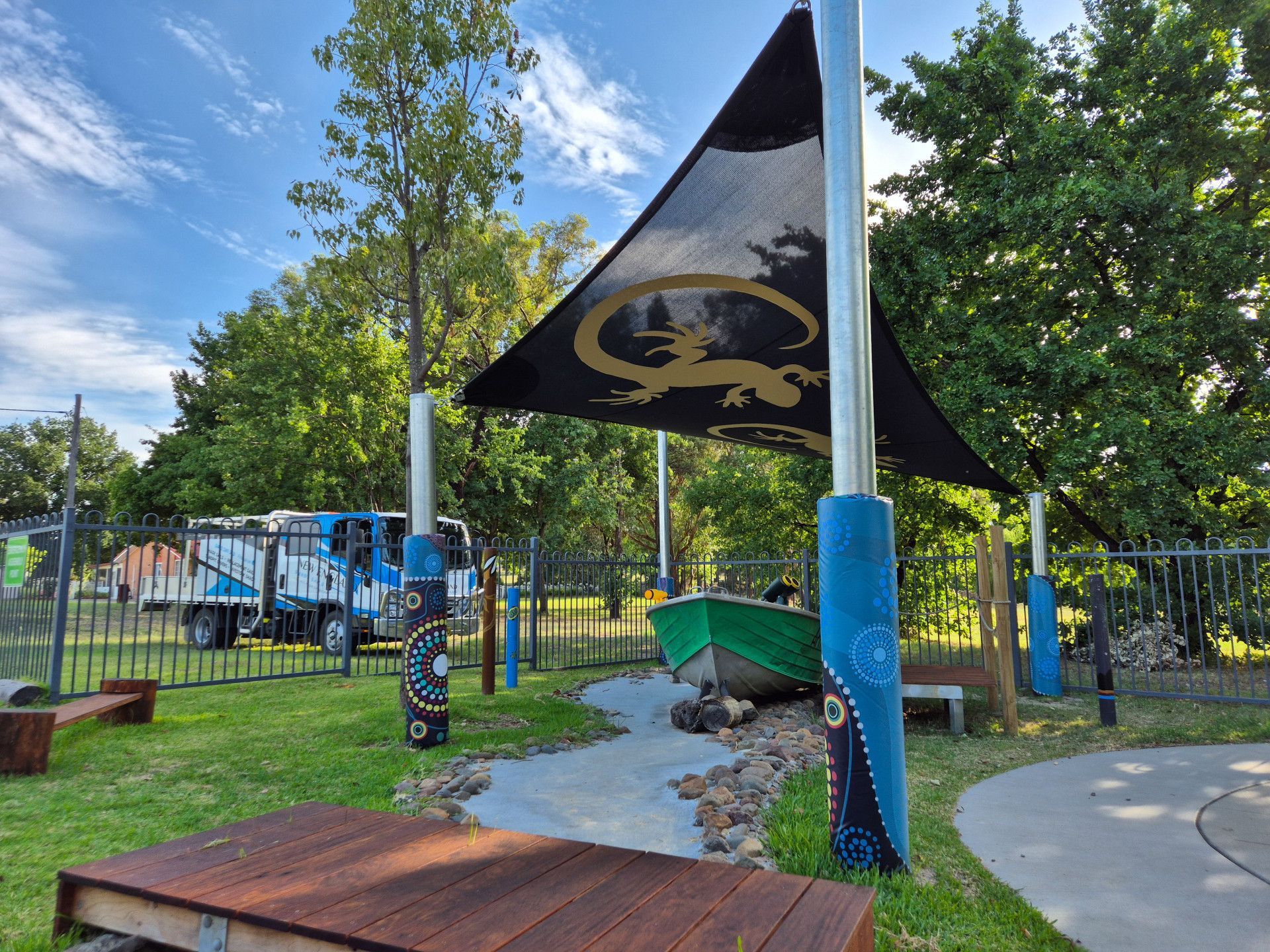 Shaded play area with Aboriginal art. Features a boat, water feature, and a truck in the background.