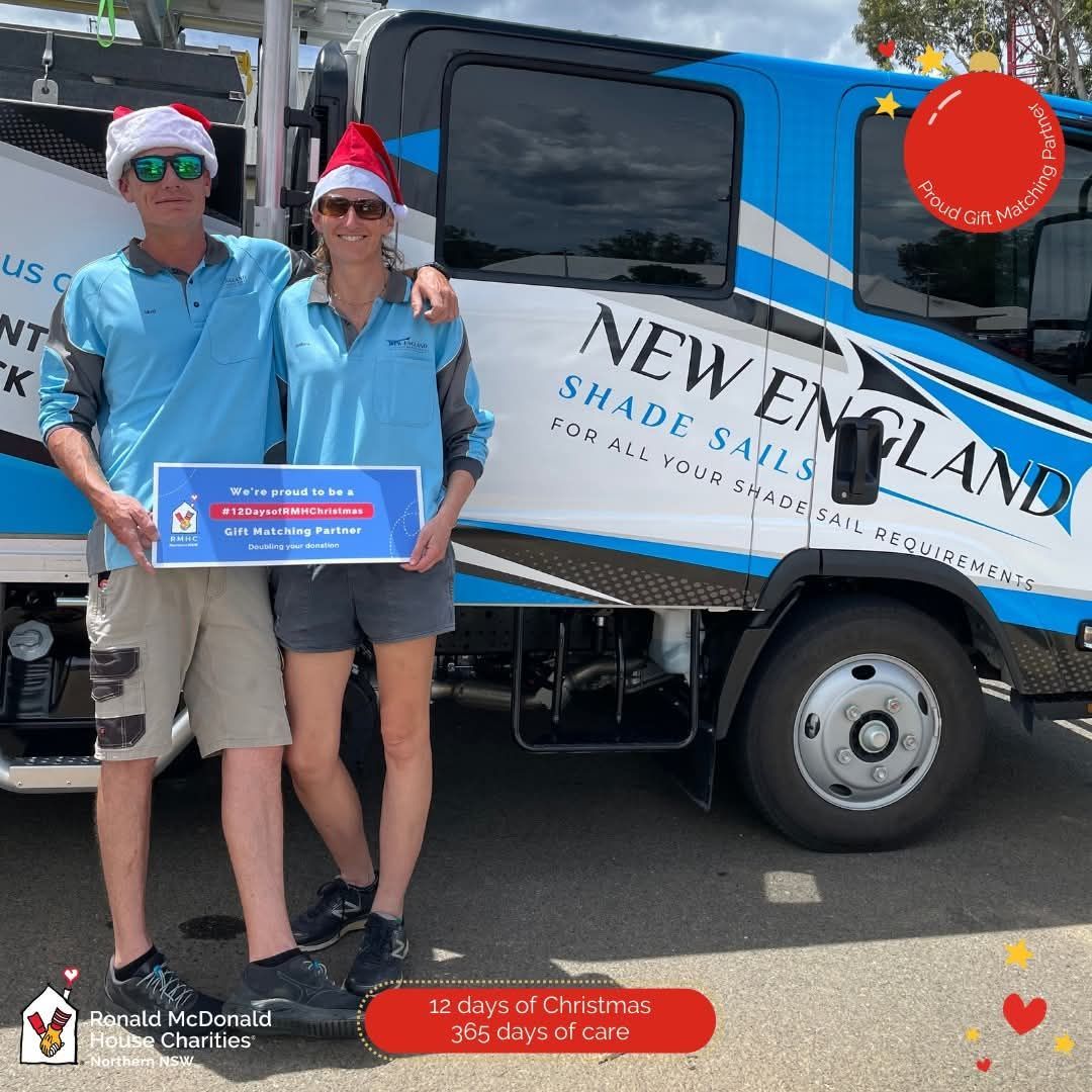 Two people in Santa hats pose with a truck, holding a sign. They are outside.