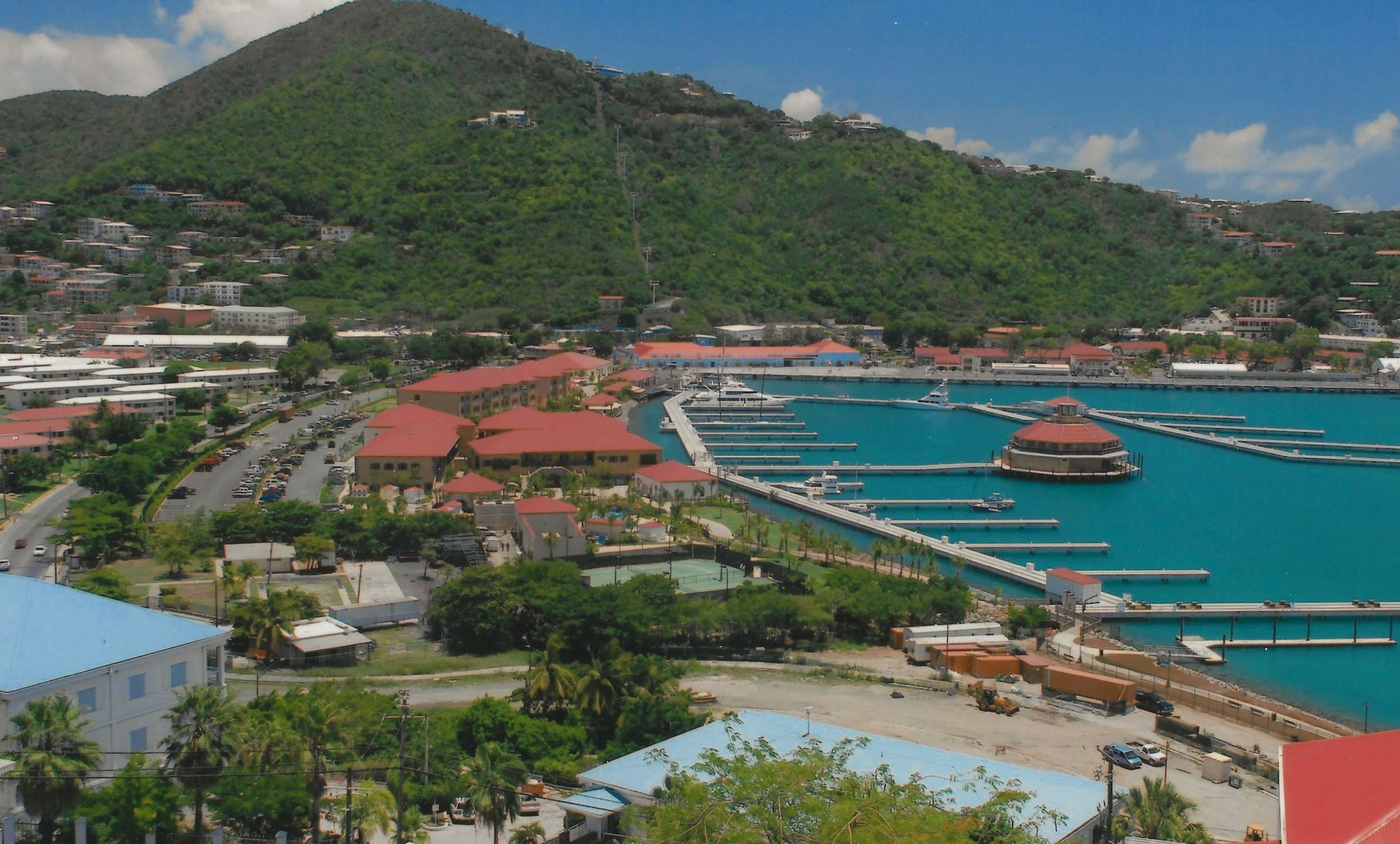 Waterfront view with a harbor, buildings, and a green mountain in the background.