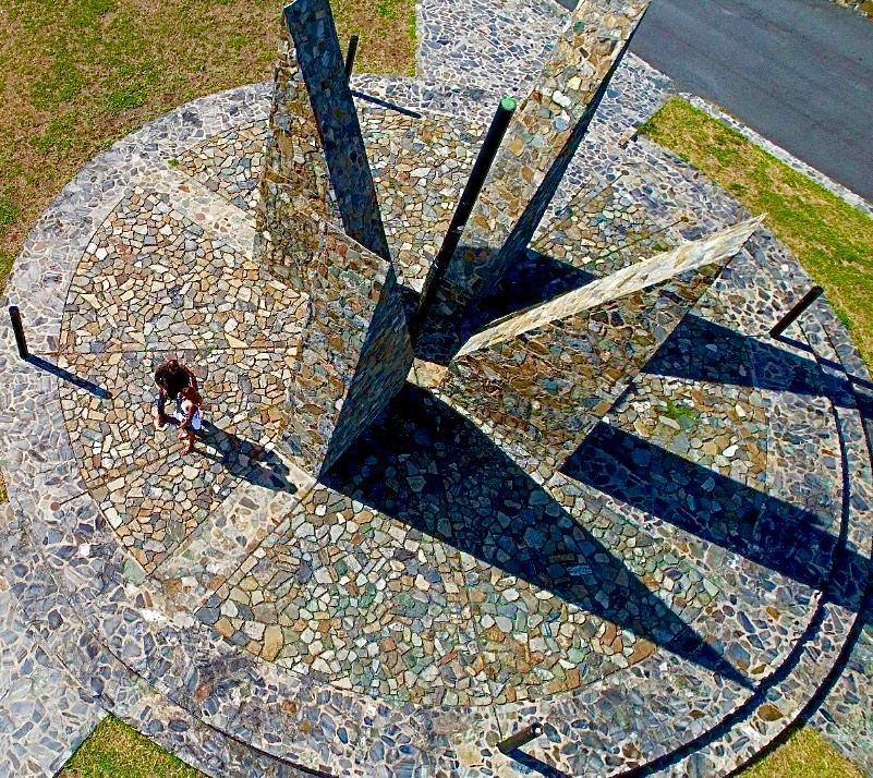 A stone sundial, casting long shadows. A person stands within the dial's circle.