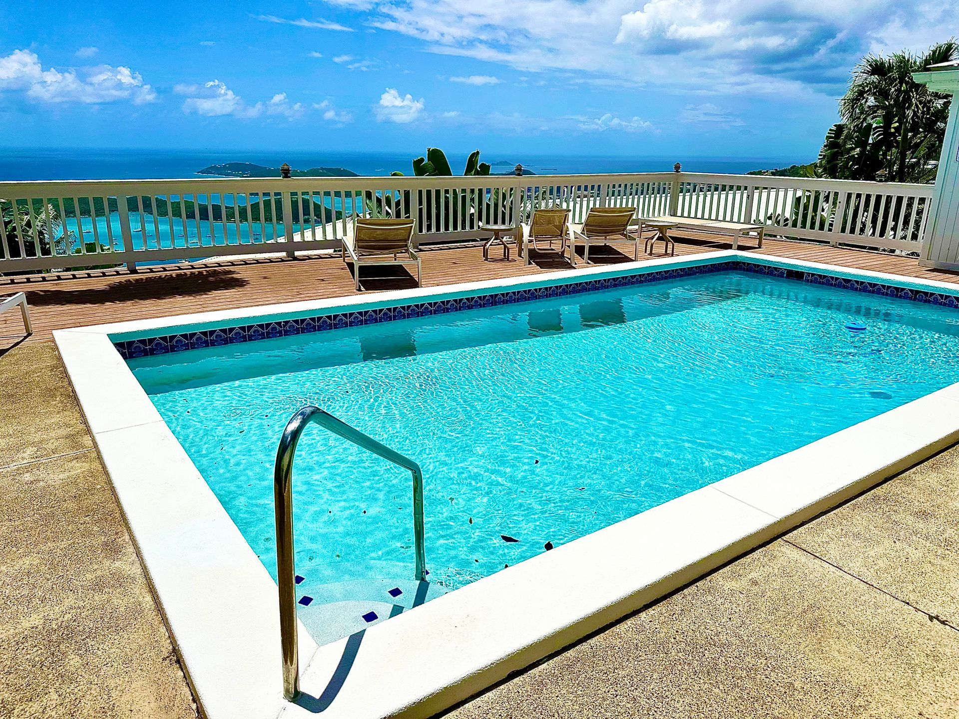 Swimming pool with ocean view, lounge chairs, and a white railing.