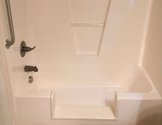 A white bathtub with a seat and a hand rail in a bathroom.