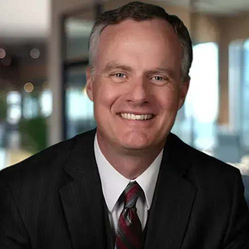 Man in a suit smiles at the camera, with a patterned tie against a blurred office background.