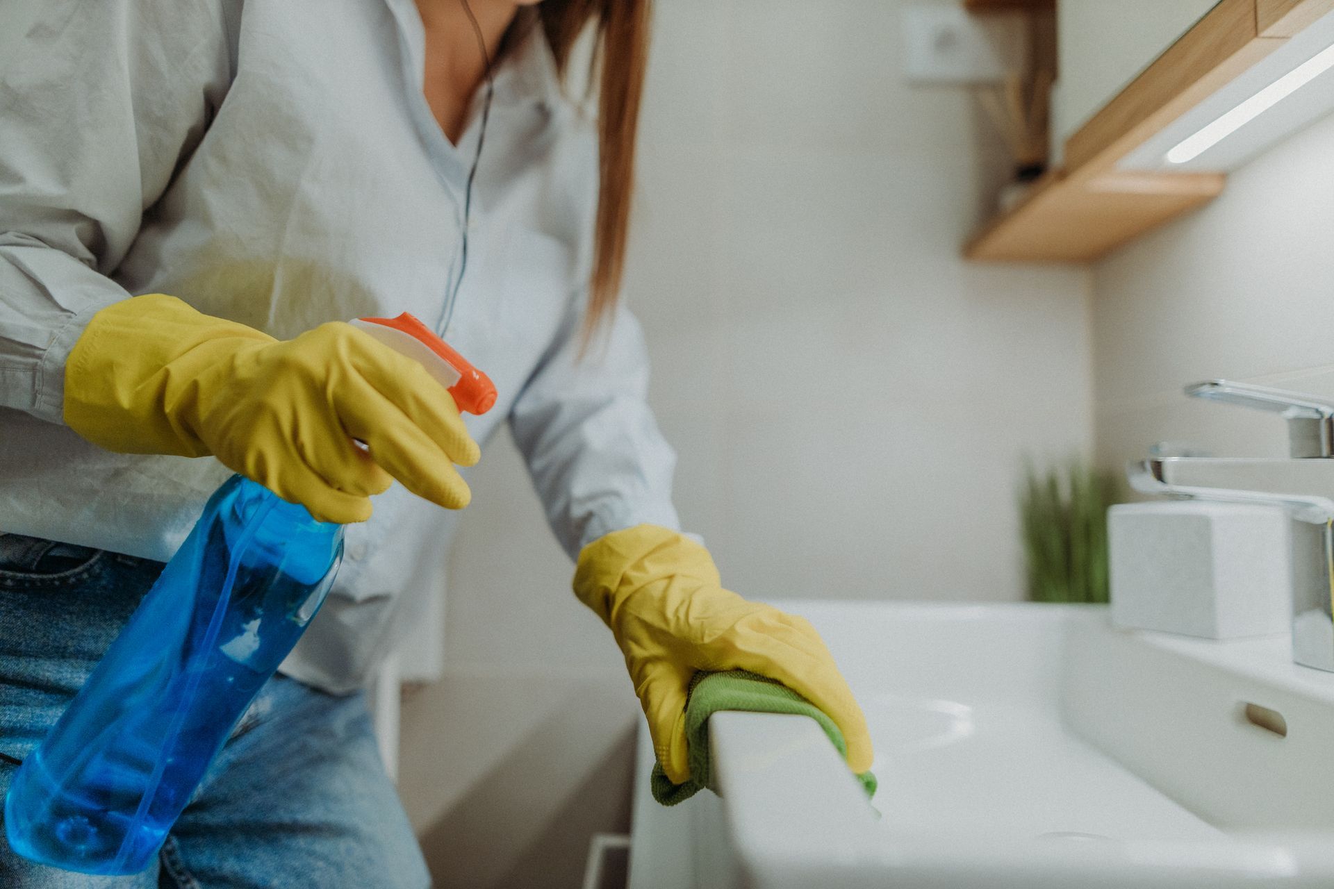 A woman wearing yellow gloves is cleaning a bathroom sink.