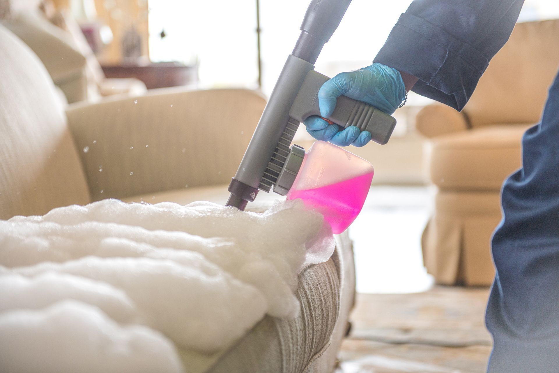 A person is cleaning a couch with a vacuum cleaner.