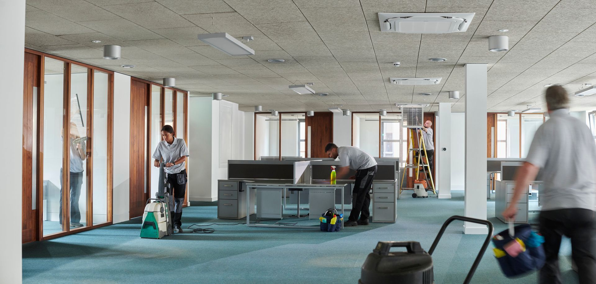 Two men are cleaning an office with a vacuum cleaner.