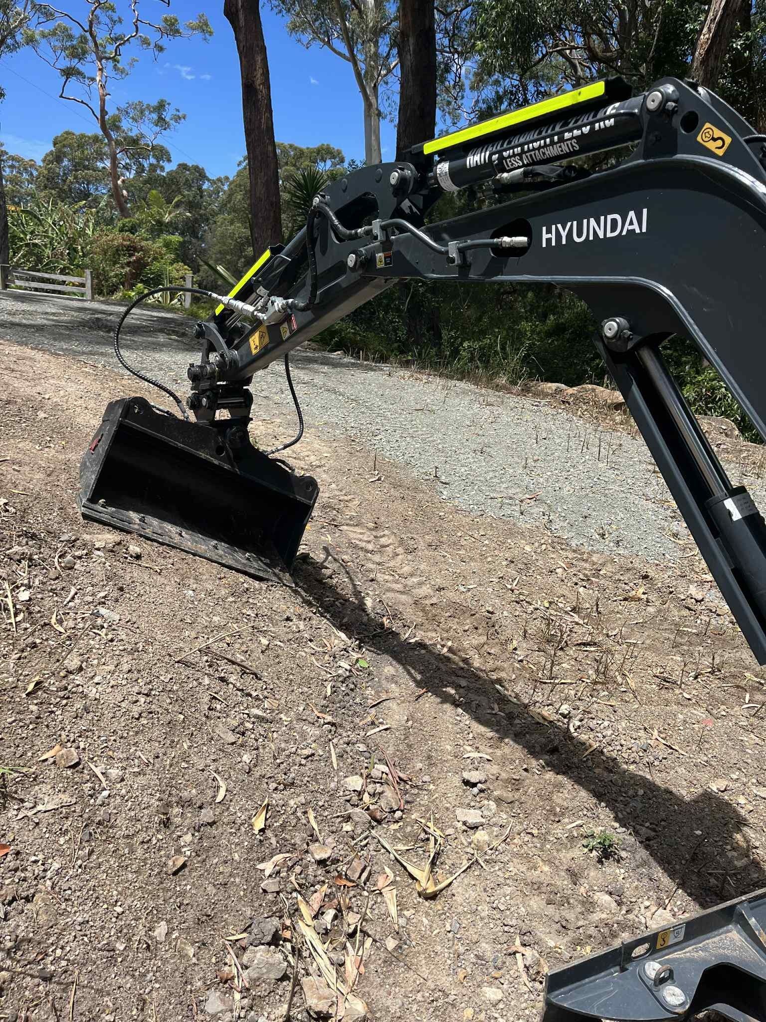 Hyundai excavator with a black bucket on a gravel path outdoors.