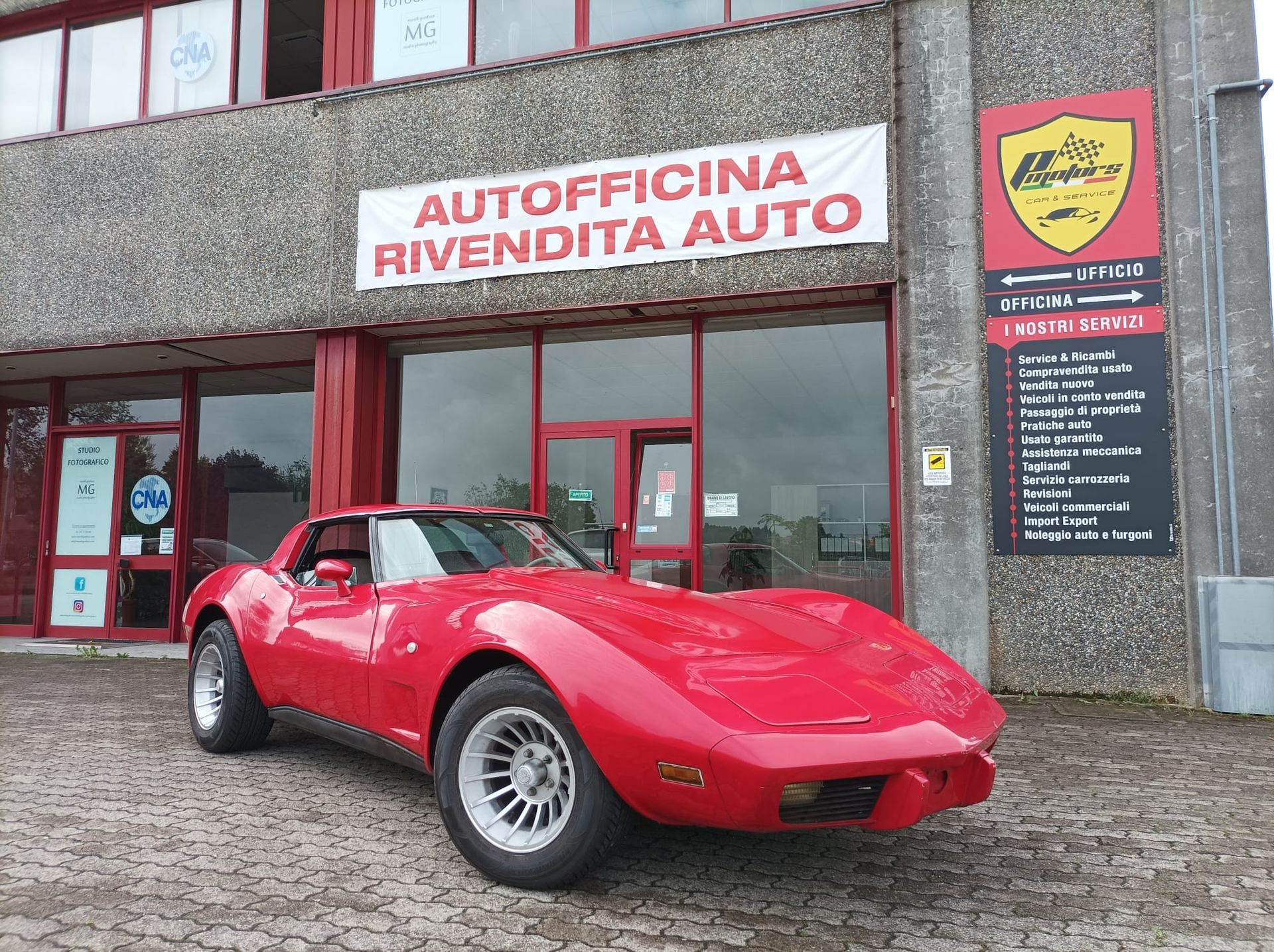 Un'auto rossa è parcheggiata davanti a un edificio con la scritta autofficina rivendita auto