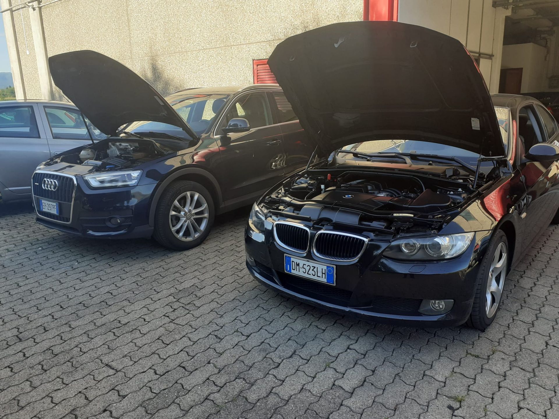 Una BMW nera con il cofano alzato è parcheggiata accanto a un'altra auto