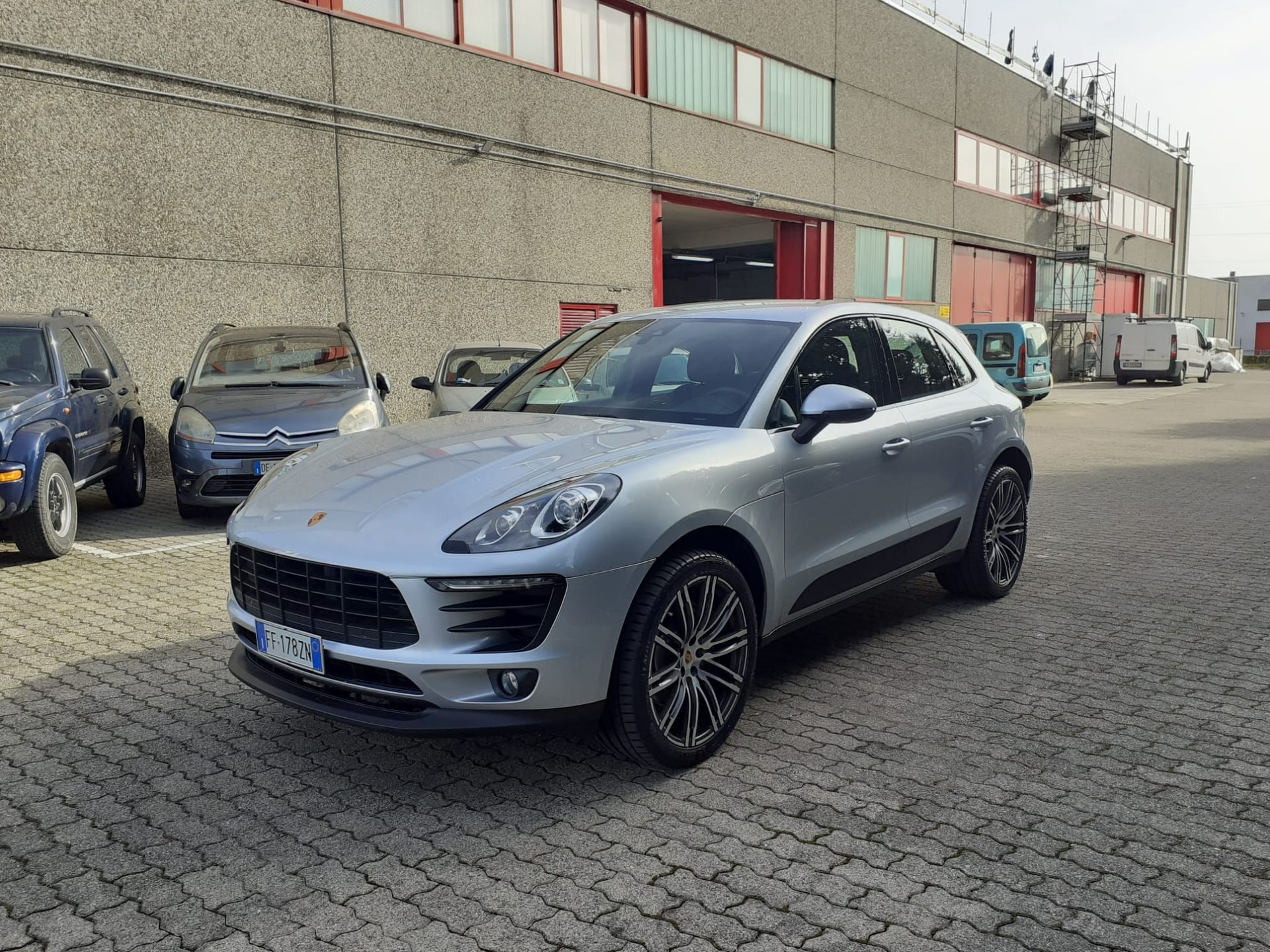 Una Porsche Macan argentata è parcheggiata davanti a un edificio