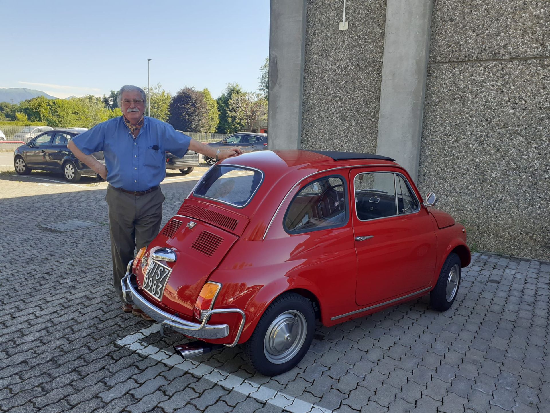 Un uomo è in piedi accanto a un'auto rossa in un parcheggio