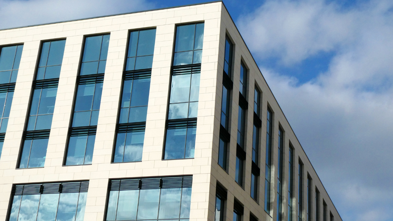 Modern office building with blue-tinted windows against a partially cloudy sky.