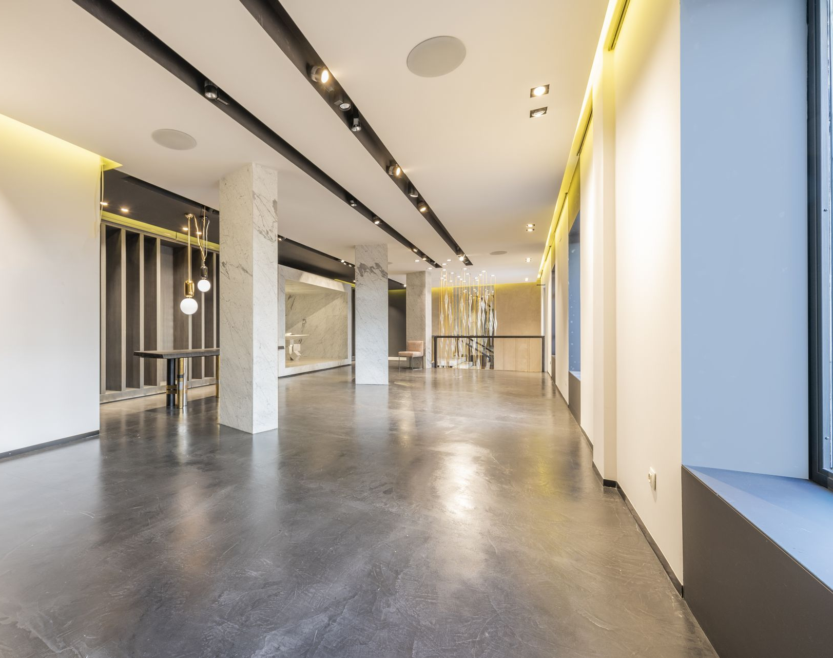 Empty modern hallway with polished concrete floor, track lighting, and tall windows.