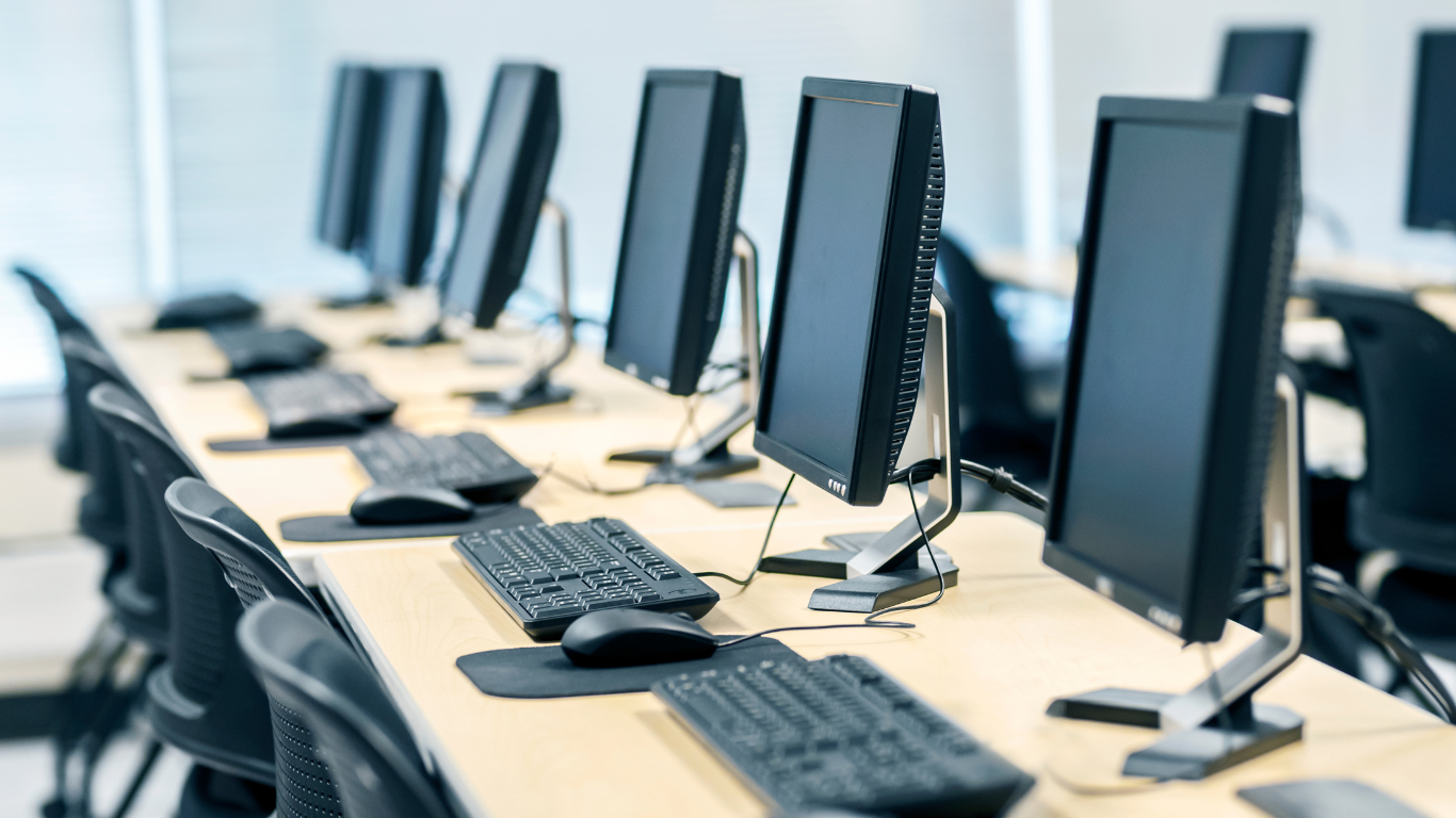 Computer lab with rows of monitors, keyboards, and mice on desks, with chairs.