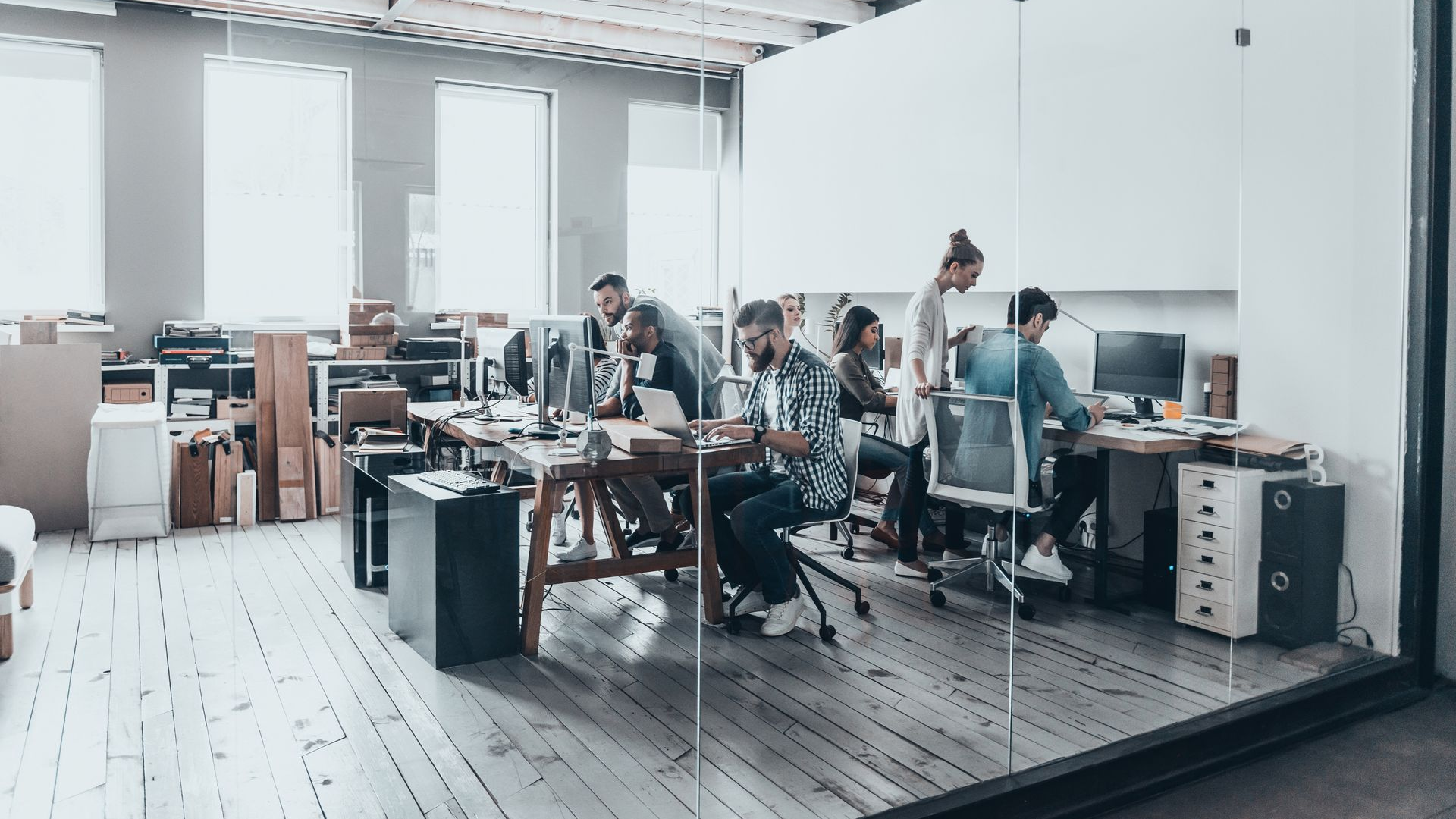 People working at desks in a modern office with glass walls, natural light.