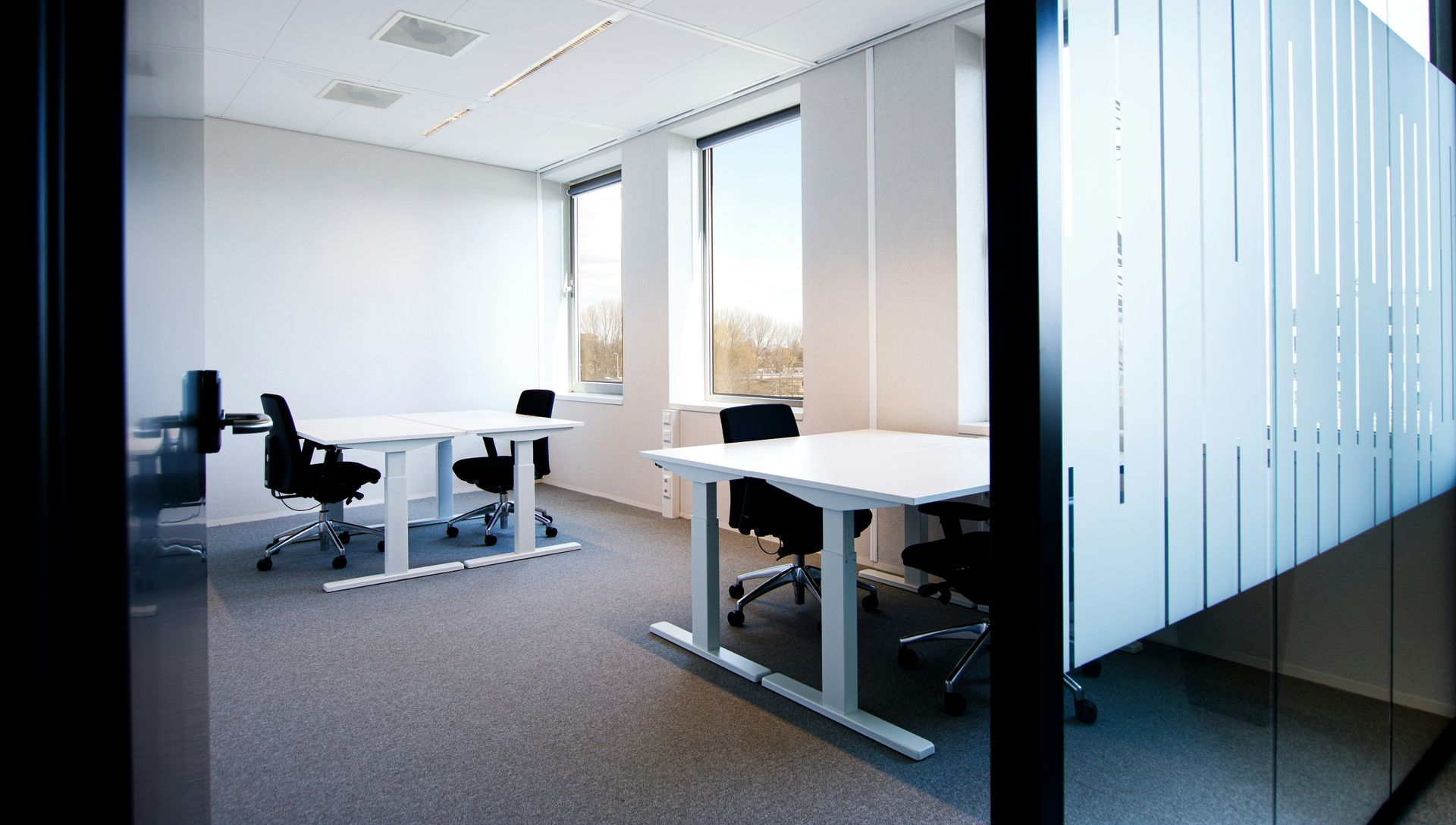 Modern office room with white tables, black chairs, and frosted glass partition.
