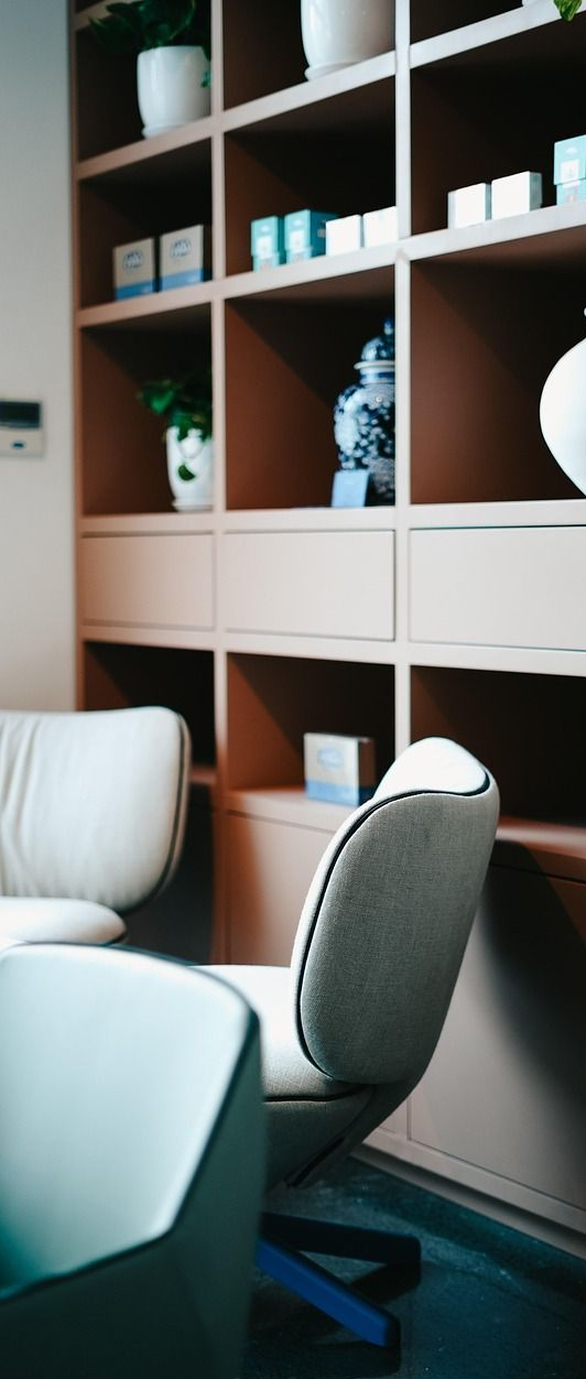A well-lit room with wooden shelves displaying various items, and a modern chair in front.