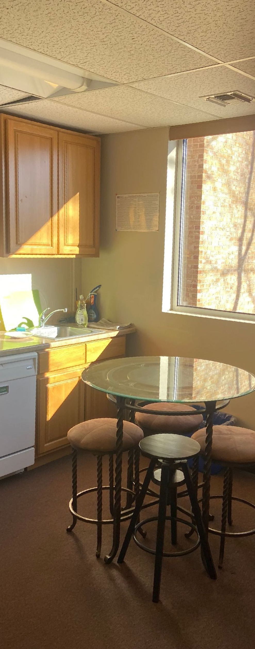 Kitchen with round table and stools, cabinets, and a window with sunlight.