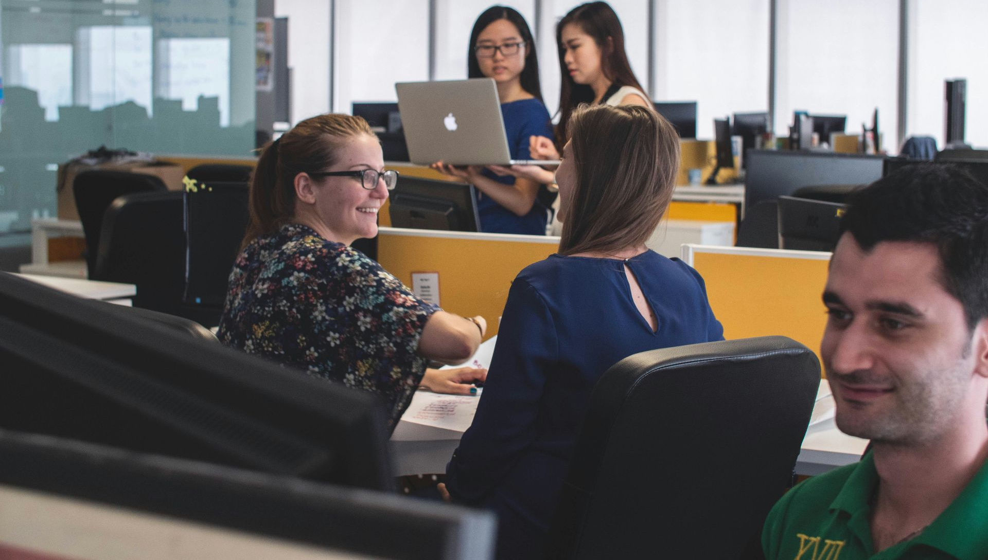 Office setting: several people collaborating around a laptop, smiling and working.