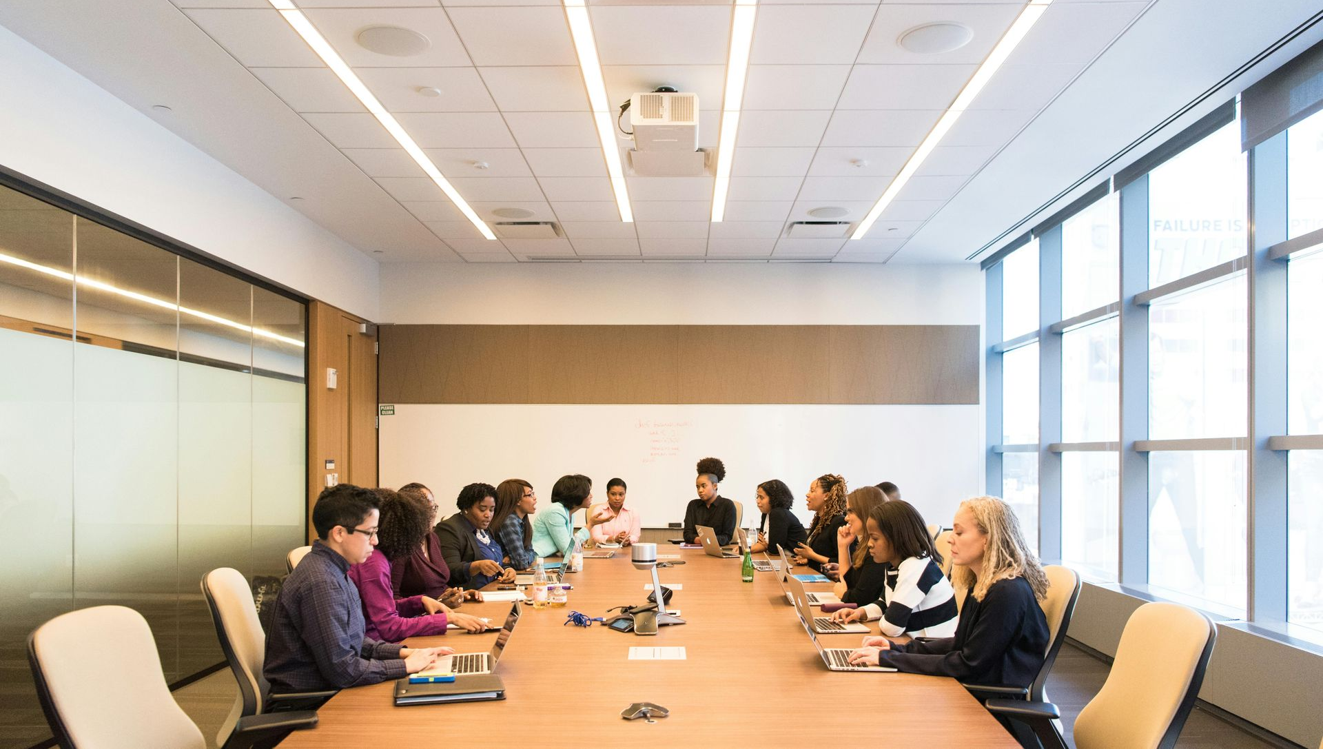 People seated around a long table in a modern conference room; engaging in a meeting.