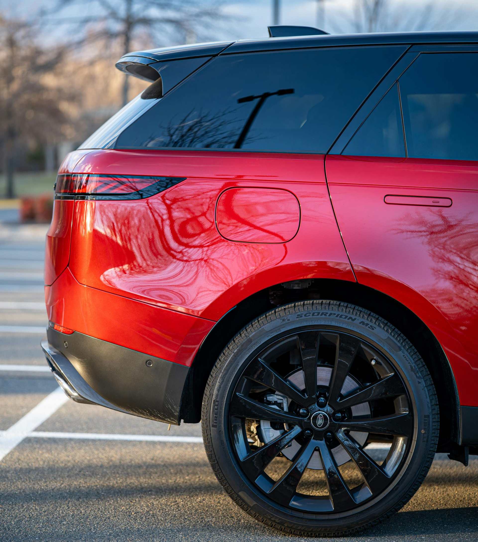 Red Land Rover SUV, black wheels and roof, parked on asphalt.