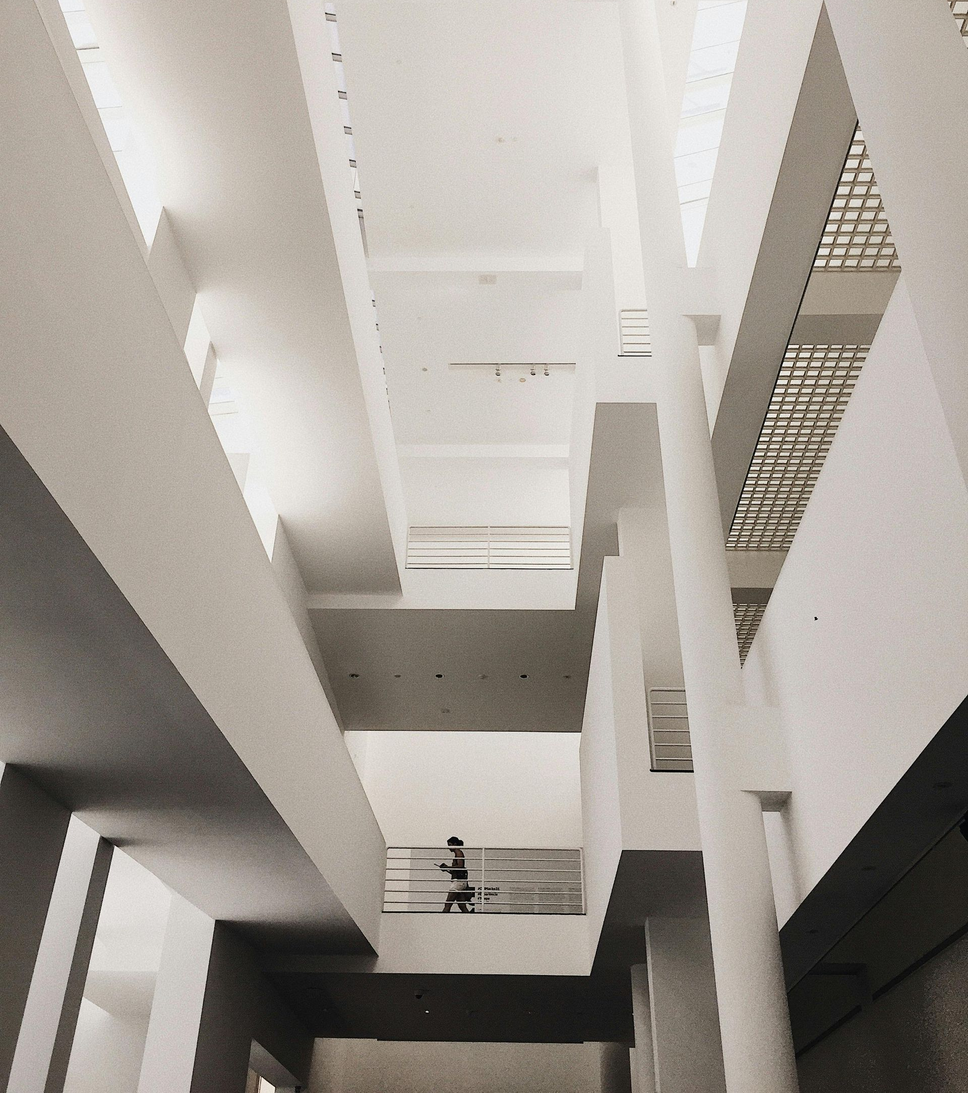 Interior view of a modern white building with geometric lines and a person on a balcony.