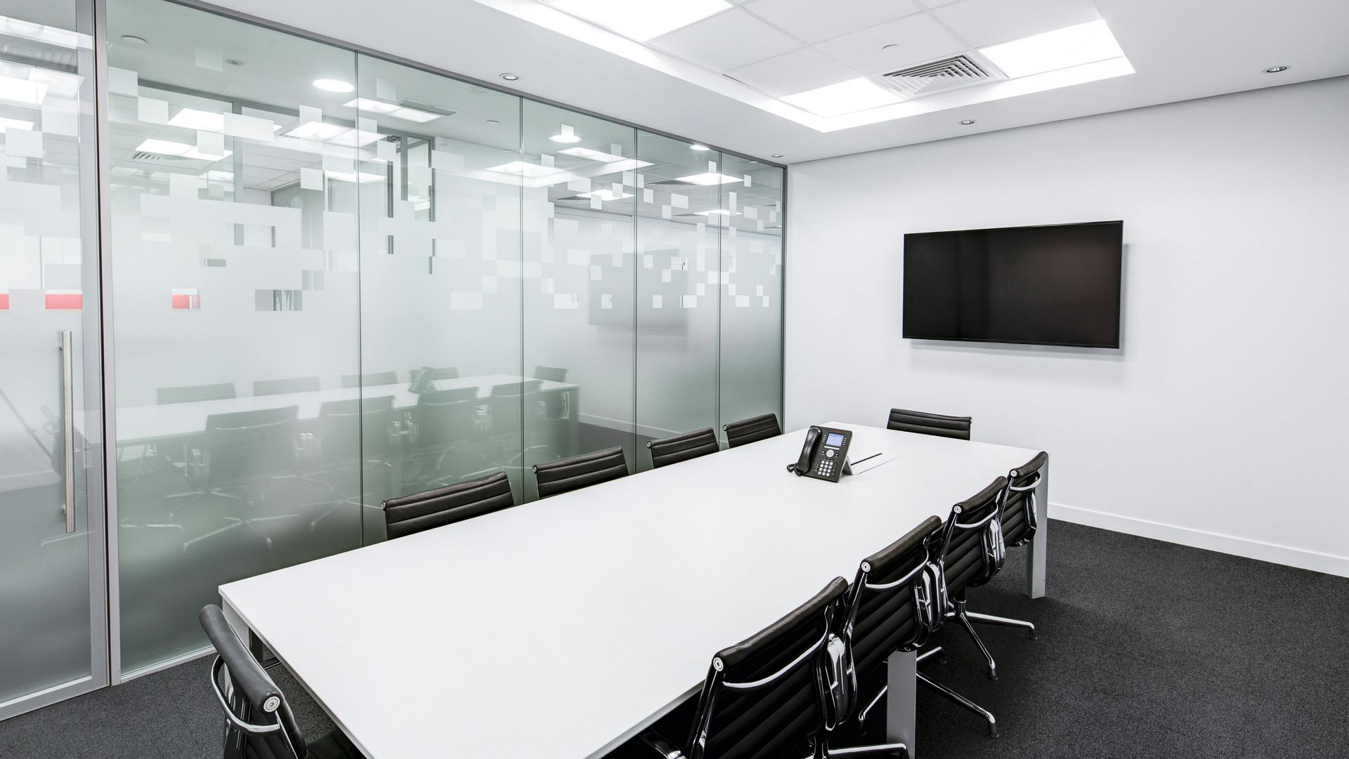 Conference room with large table, chairs, and frosted glass wall. A mounted TV is on the wall.