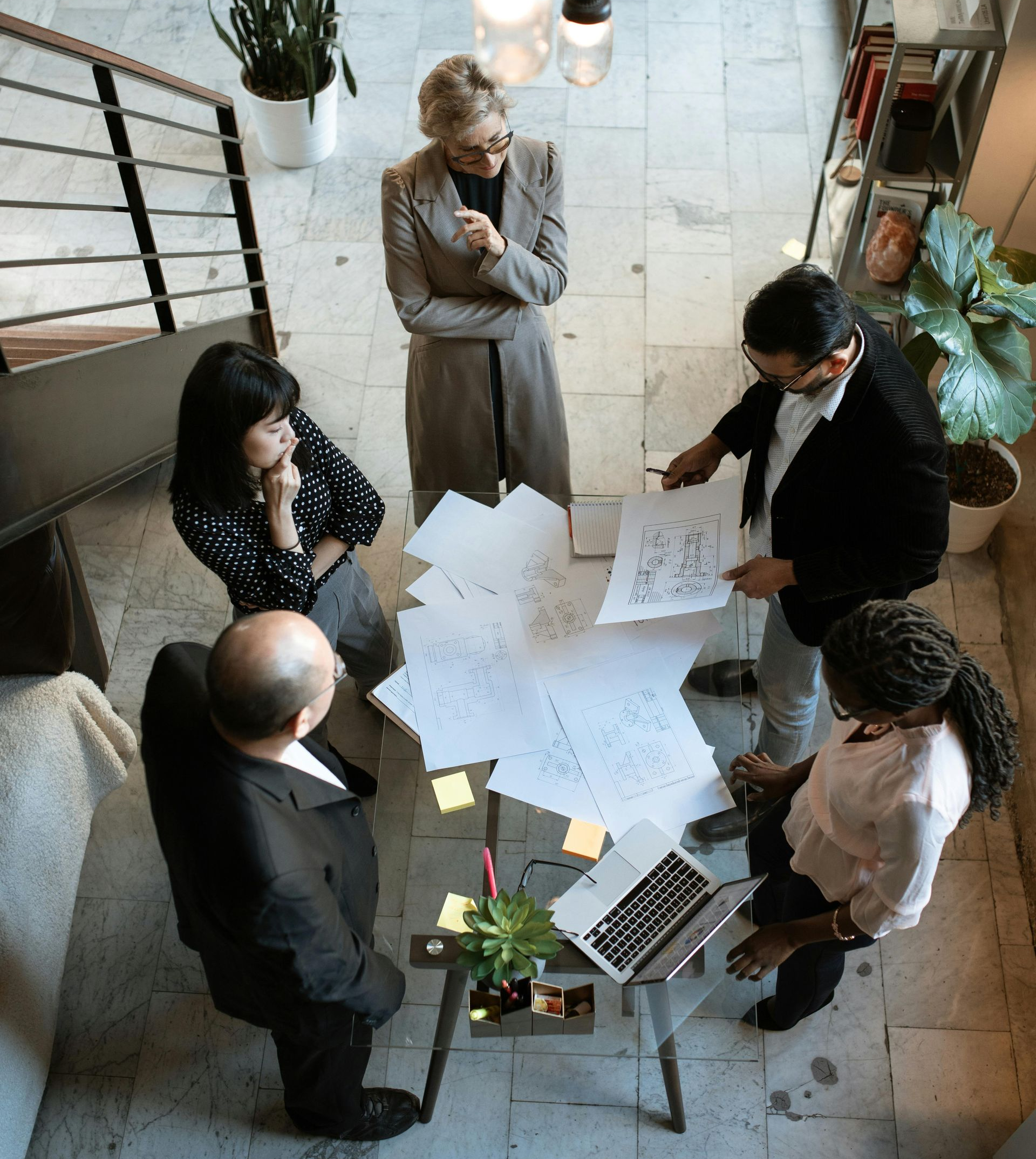 Five people in business attire reviewing papers around a table with a laptop.