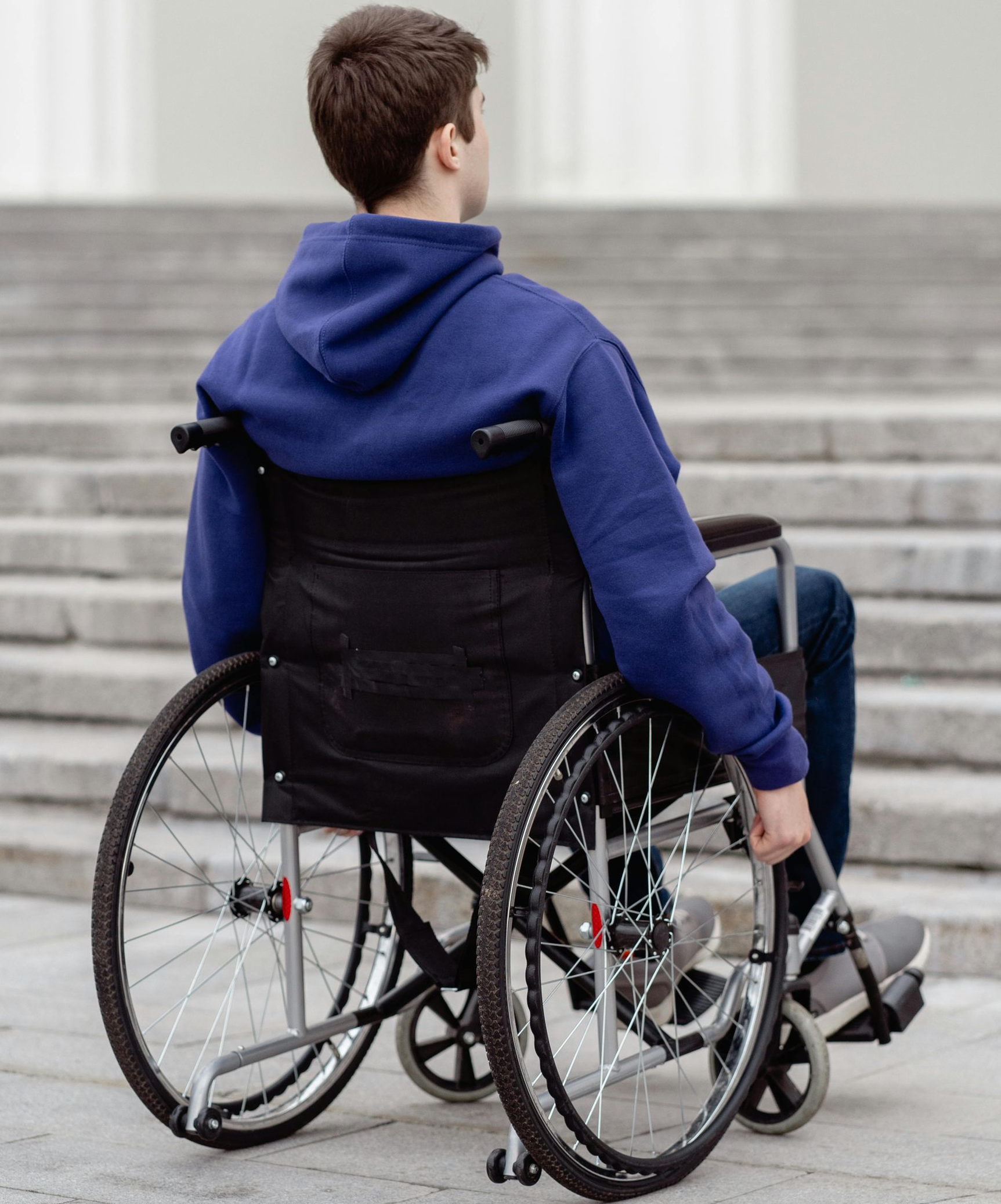 Person in wheelchair facing away from camera, near outdoor stairs.