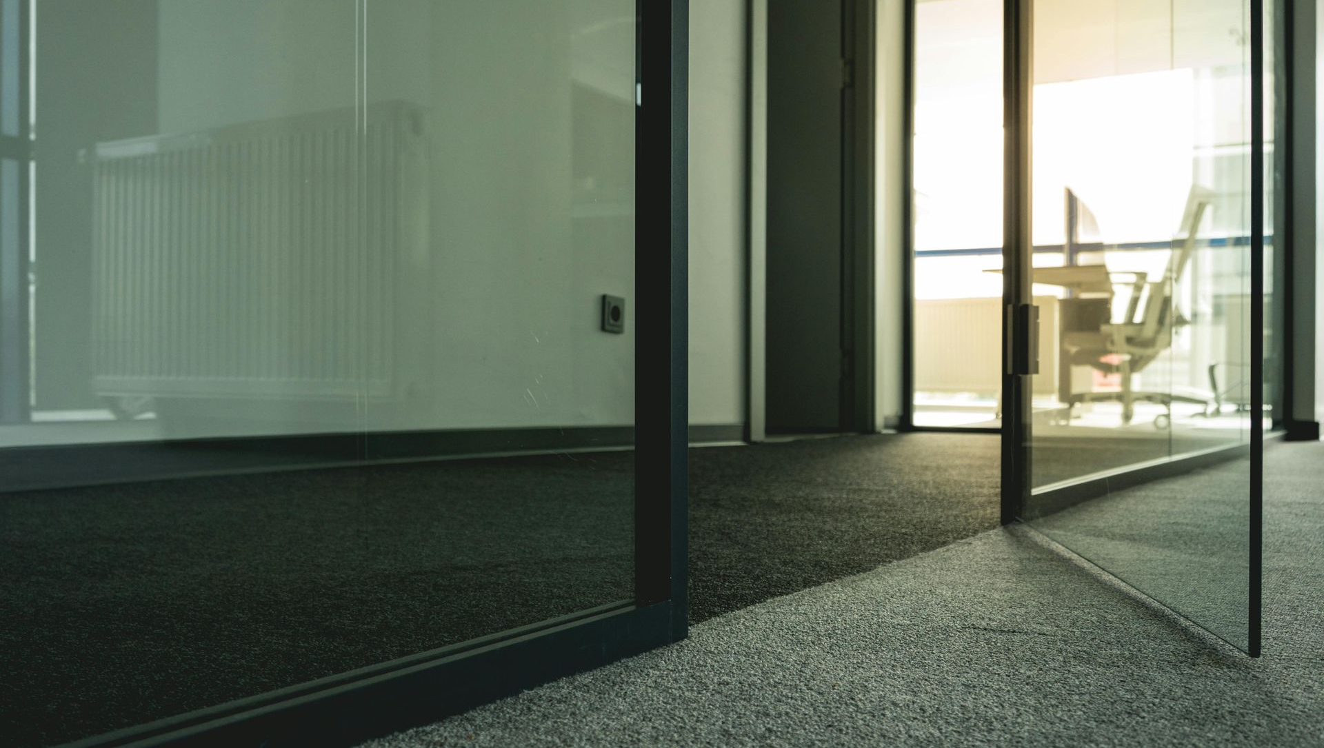 Glass office walls with a view of a desk and chair; carpeted floor.