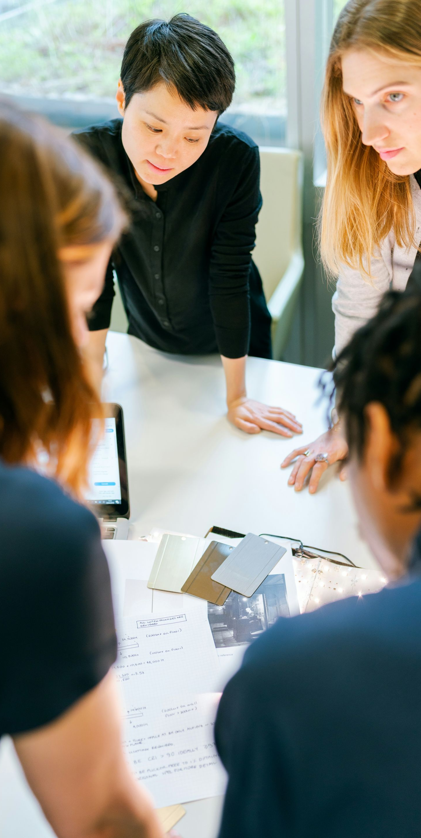 People gathered around a white table, reviewing documents and samples. Indoor setting with daylight.