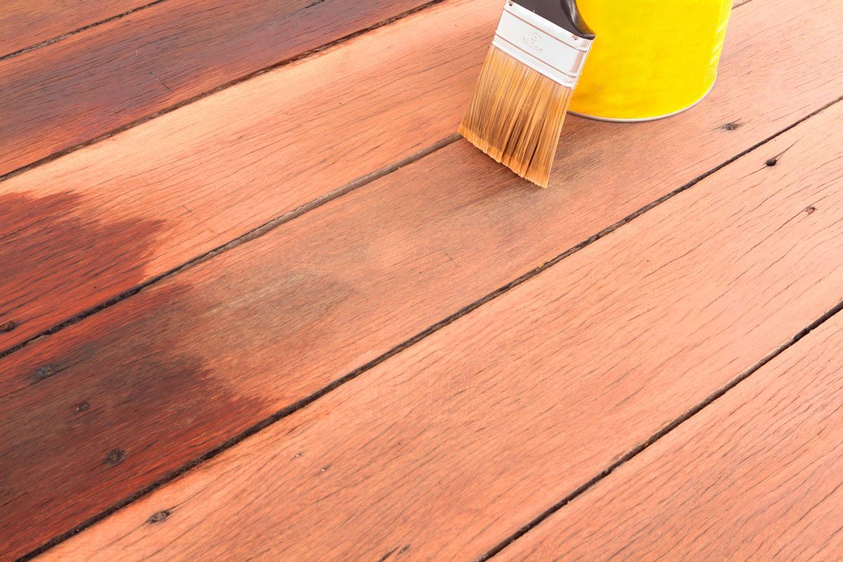Wooden deck boards being stained, brush and yellow can visible.