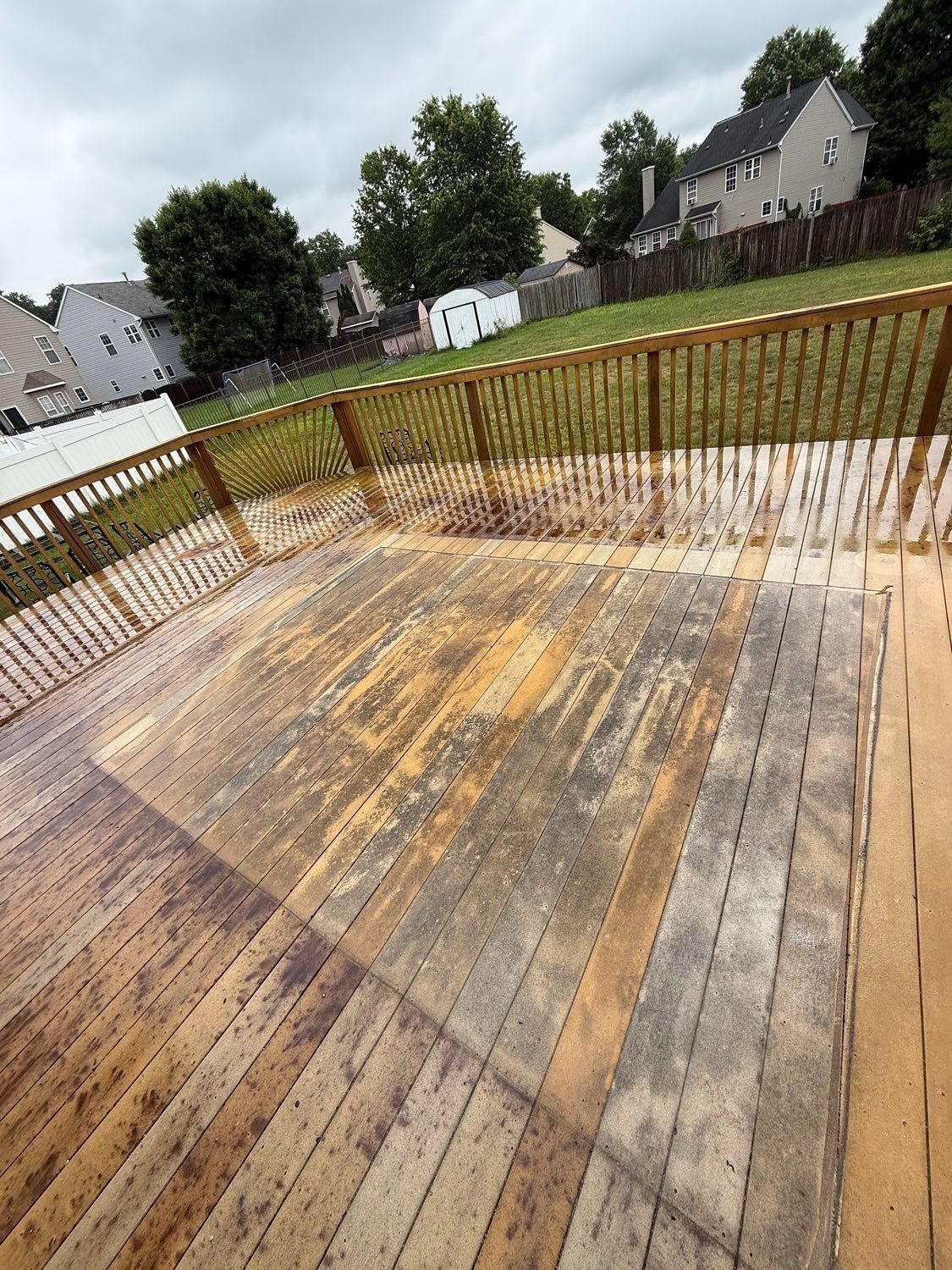 A wooden deck in progress showing a partially power-washed section contrasting with older, weathered, gray wood.