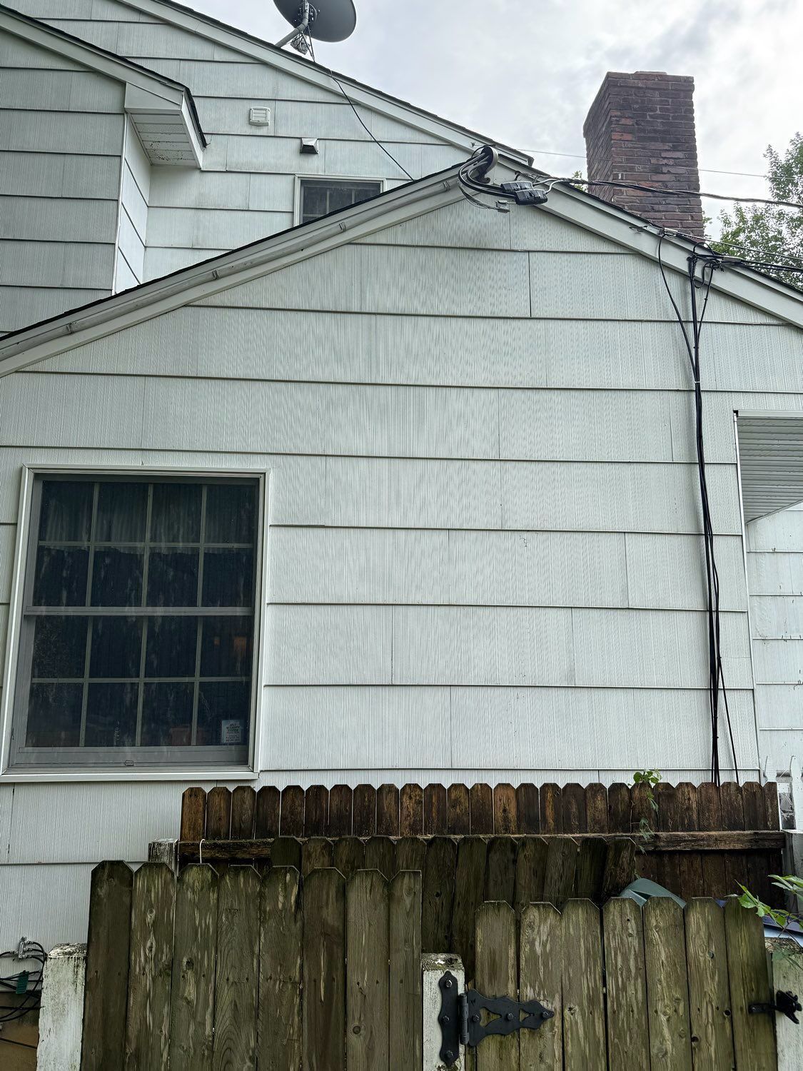 A white house exterior featuring horizontal siding, a window, a brick chimney, and a wooden fence in the foreground.