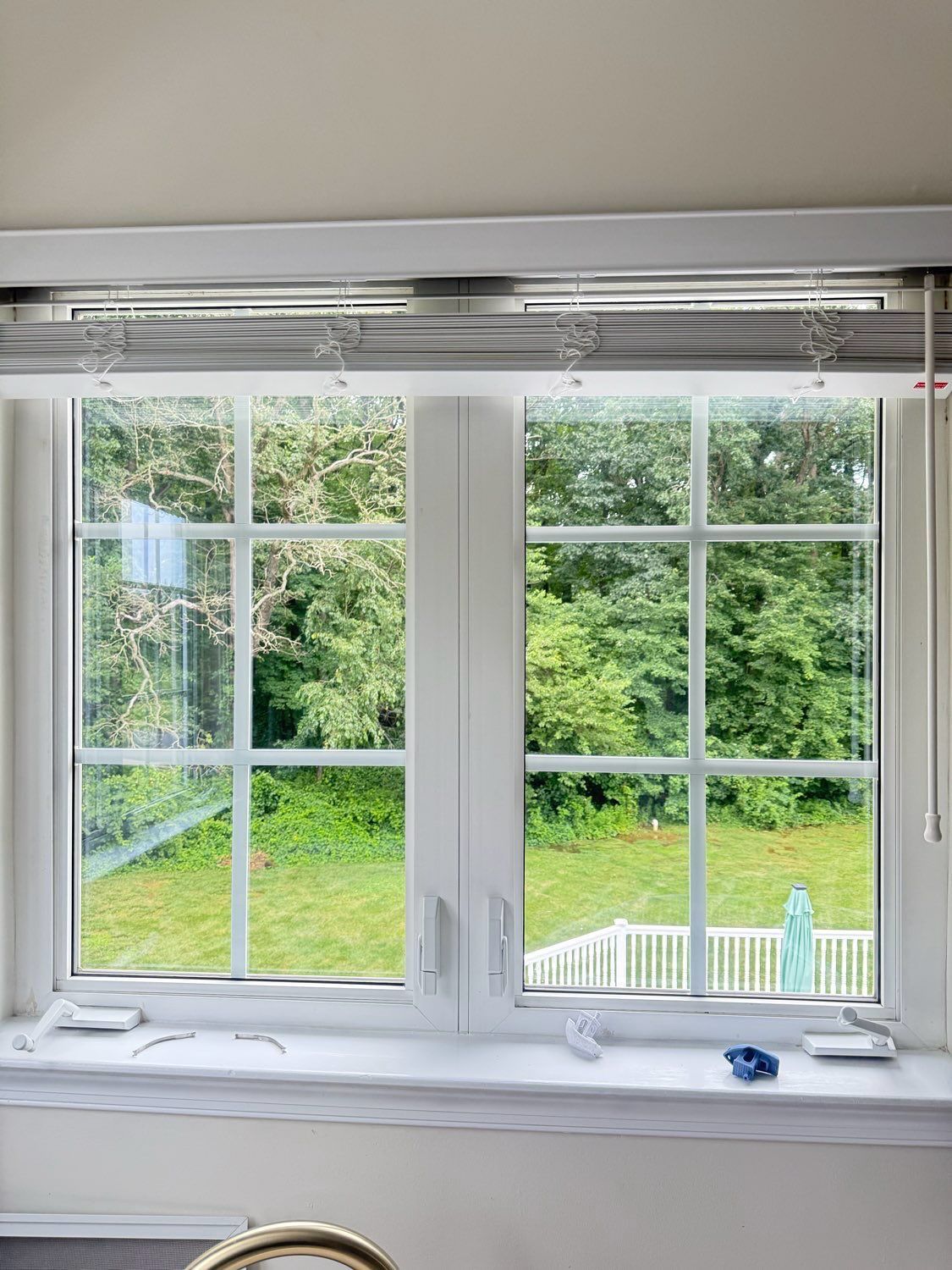A white-framed double window looking out onto a grassy yard with trees and a white railing in the background.