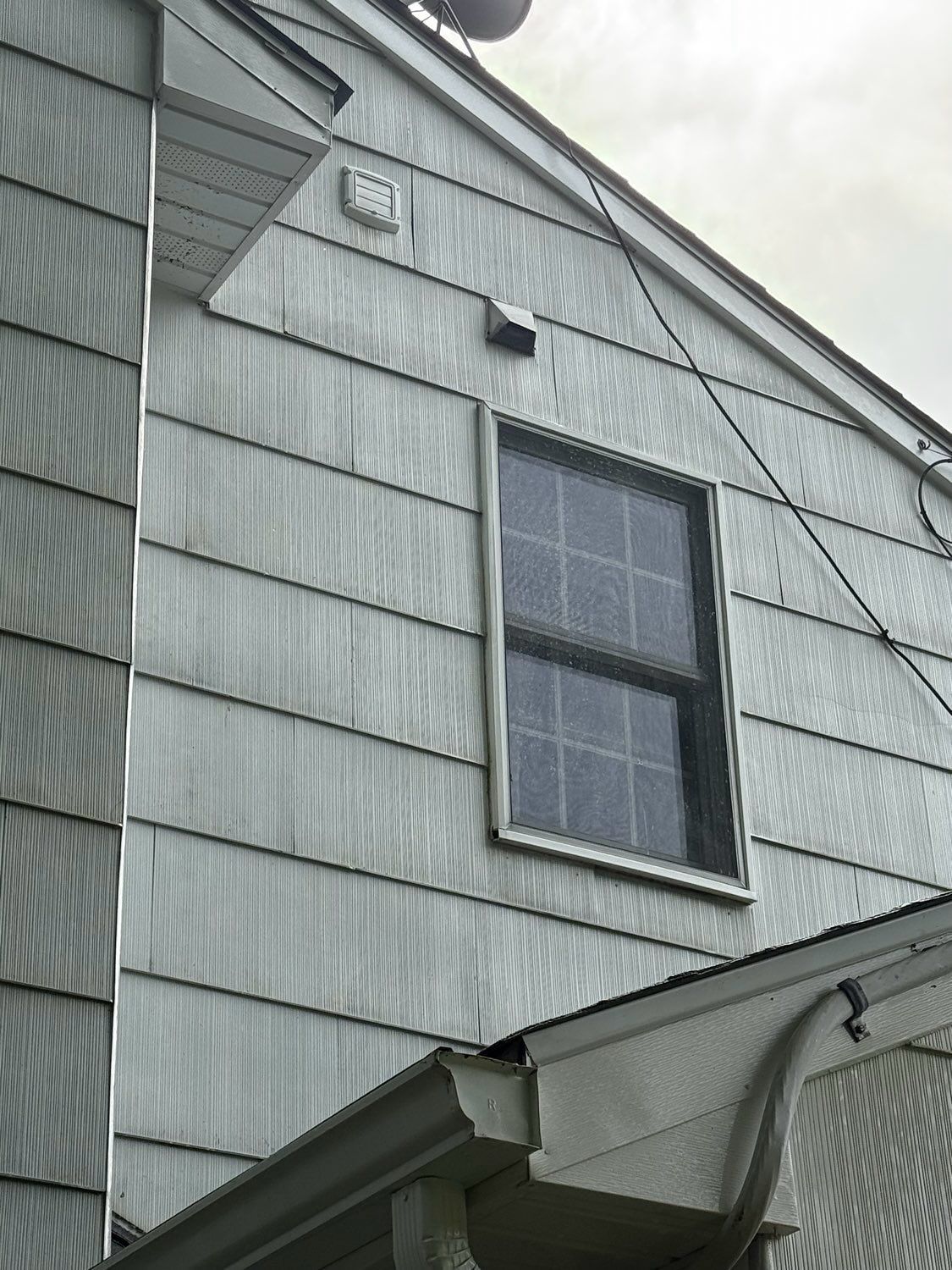 An exterior wall of a building covered in gray siding, featuring a window and two small vents under a gabled roof.