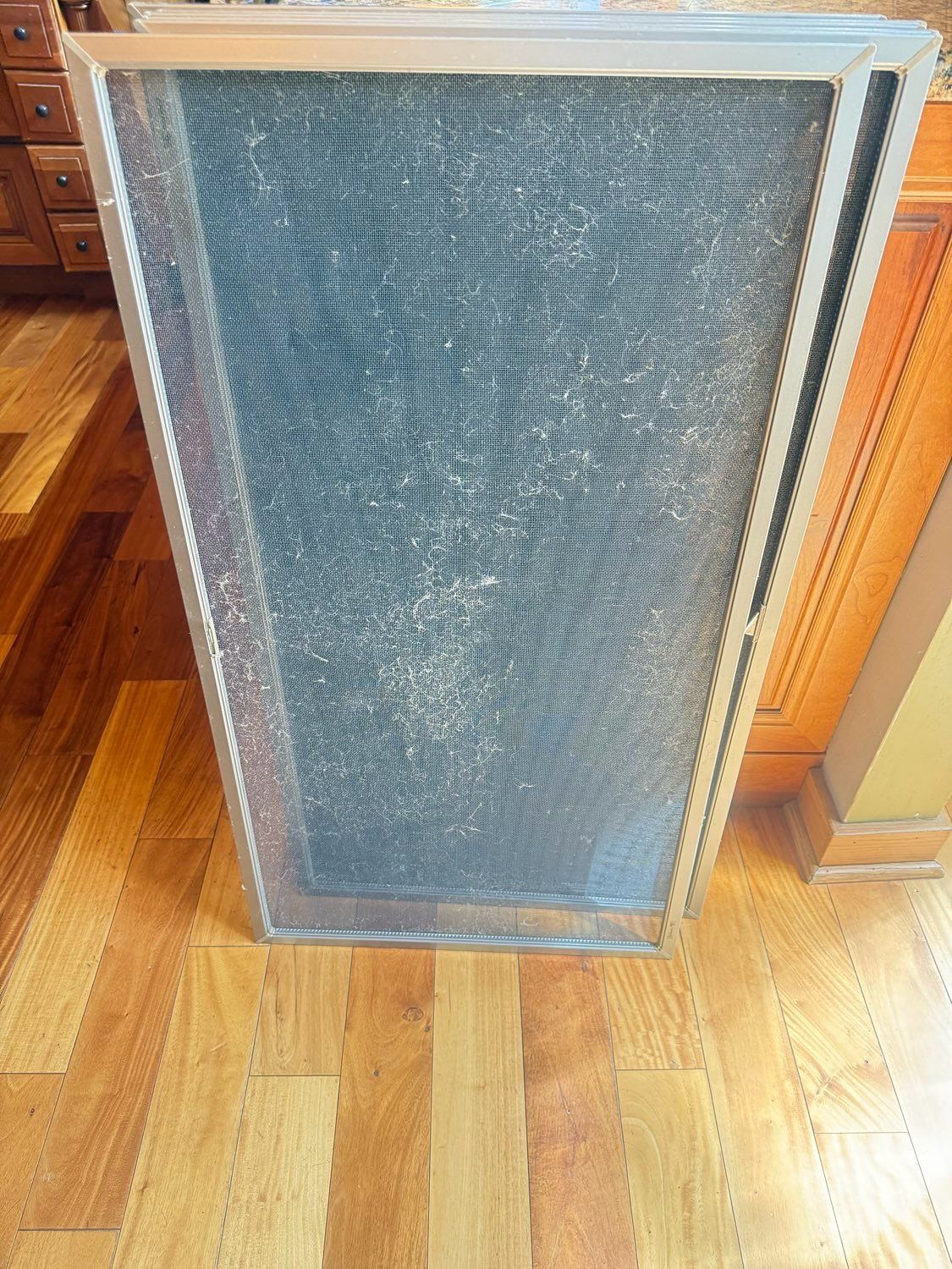 A rectangular air filter with a metal mesh frame standing upright on a hardwood floor.