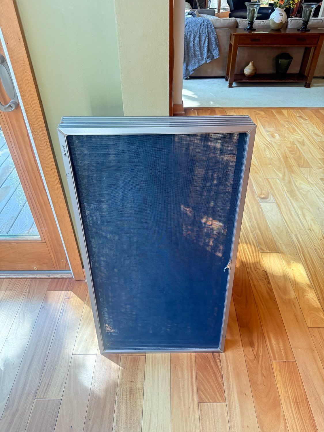 A rectangular air filter with a dark blue mesh material and a metallic silver frame standing on a wooden floor.