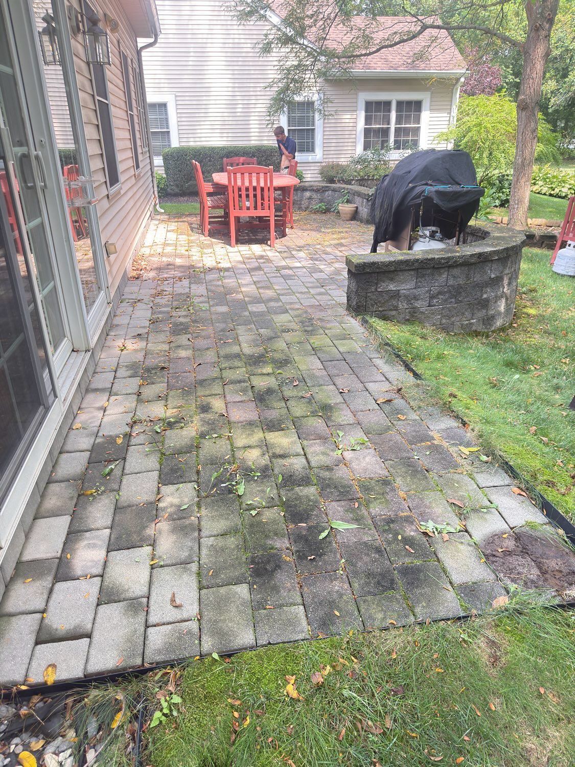 A patio with weathered grey stone pavers leading to a small outdoor dining area with a red table and a covered grill.