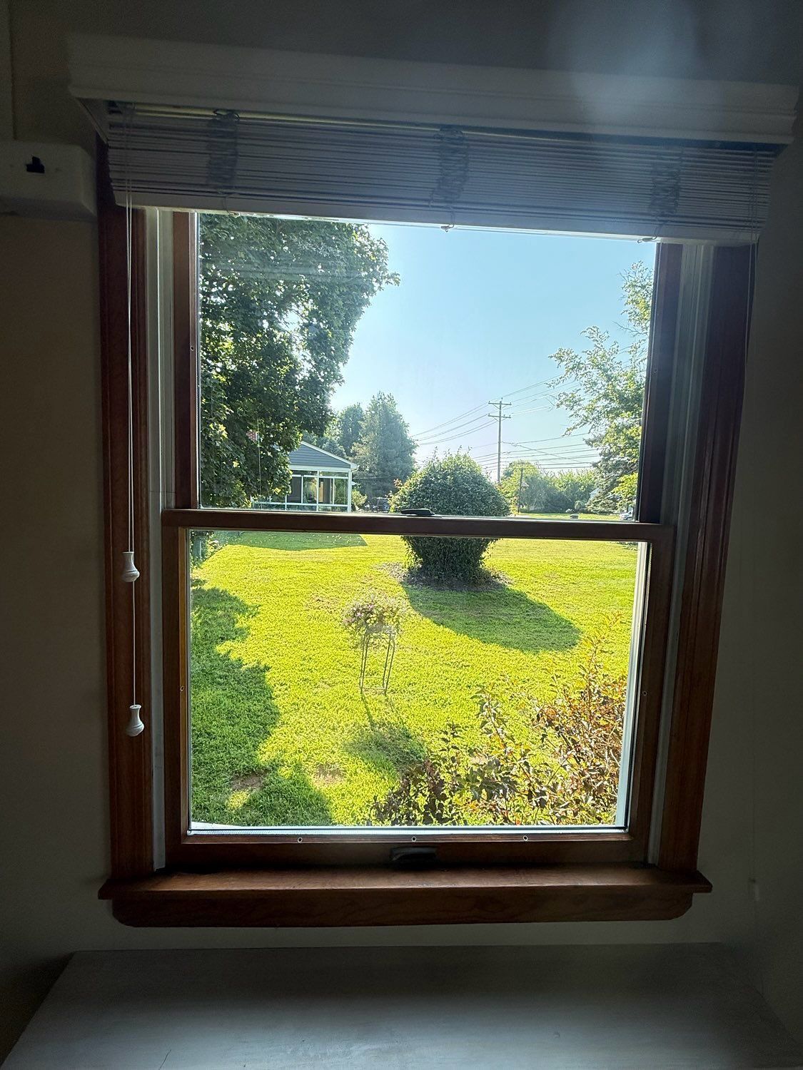 A view through a wooden window frame looking out at a sunny green yard with a gazebo in the distance.